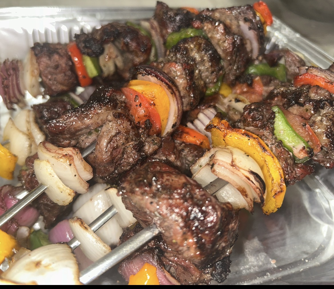 Skewers of grilled meat with vegetables including bell peppers and onions on a tray.