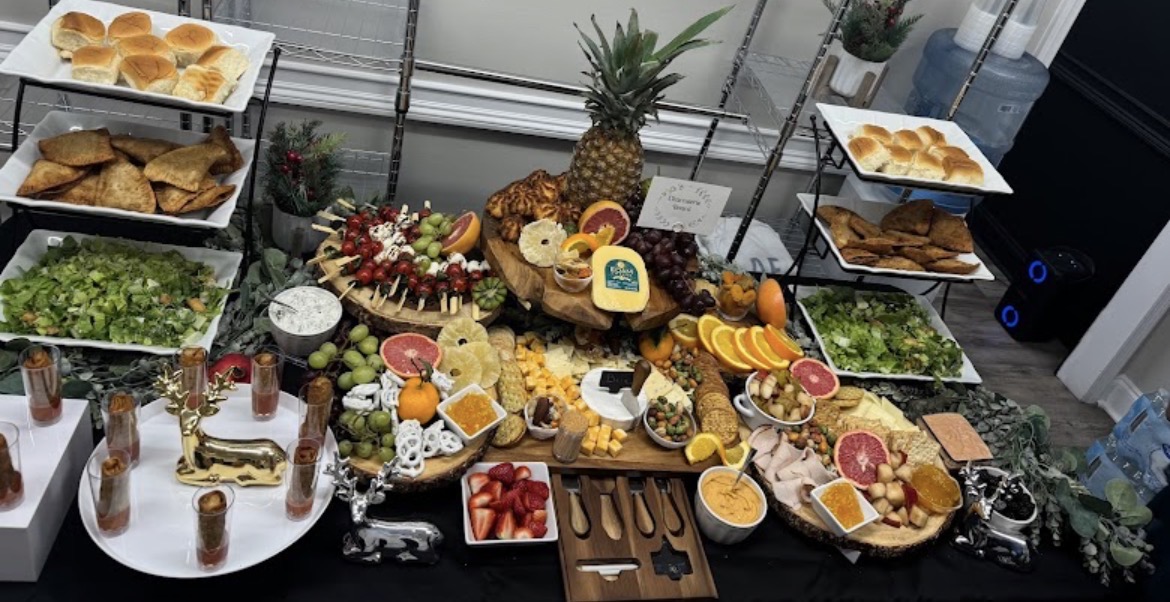 Assorted fruits, pastries, and snacks arranged on a table with a pineapple centerpiece, including sliced oranges, strawberries, and cookies.