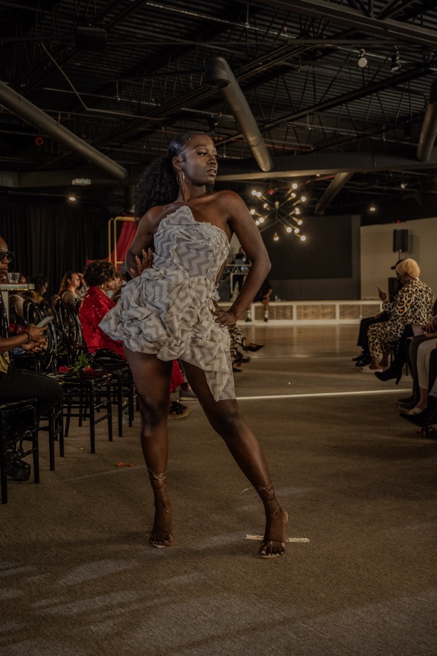 Woman dancing in a large indoor space with seated audience, stage, and string lights in background.