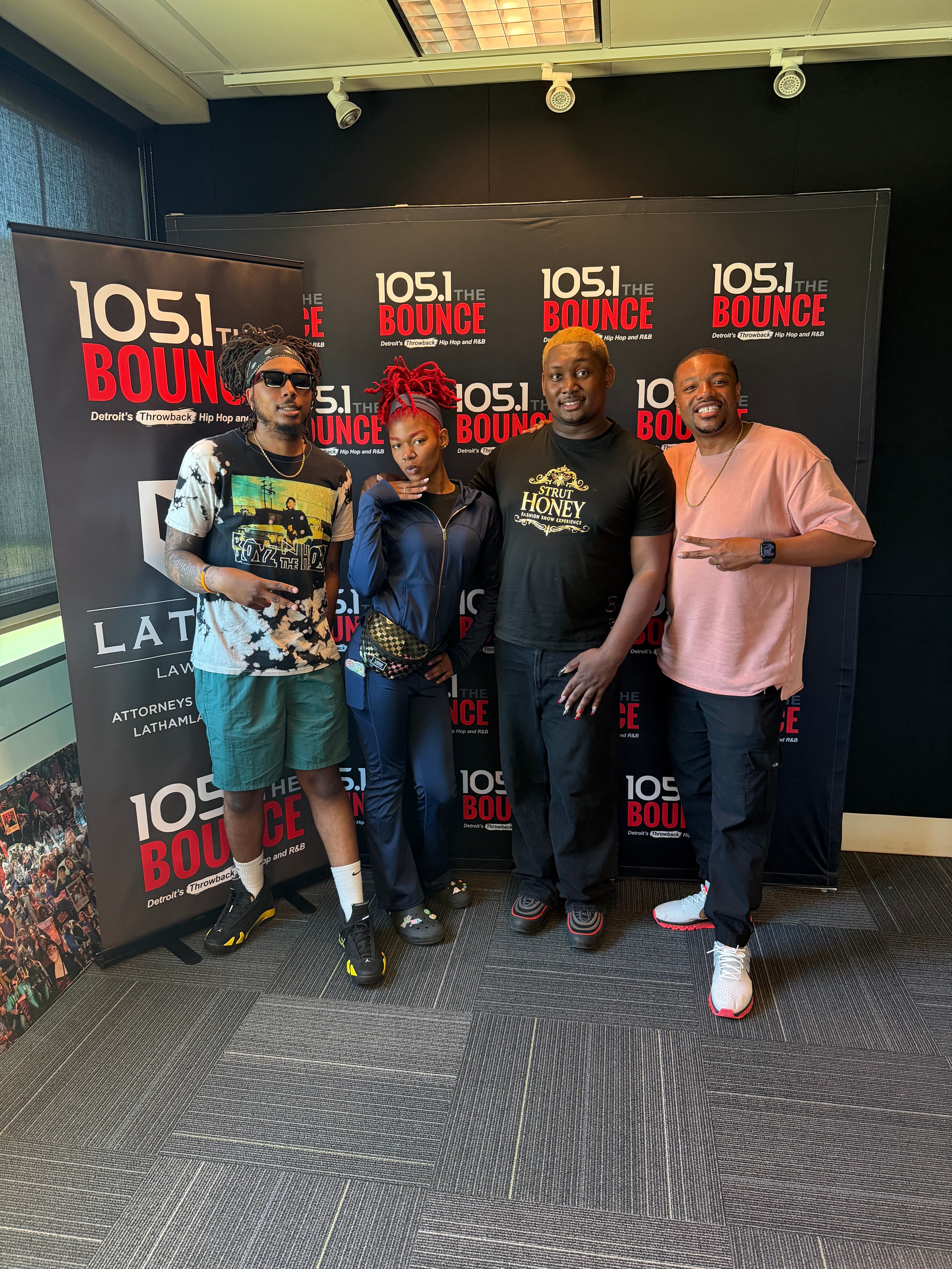 Four people standing in front of a promotional backdrop, holding a magazine, in a room with gray carpeted floor.