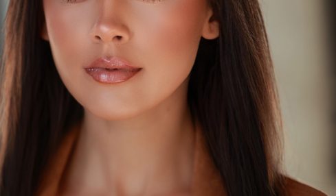 Close-up portrait of a woman with long dark hair, makeup, and a neutral expression, wearing a brown top.