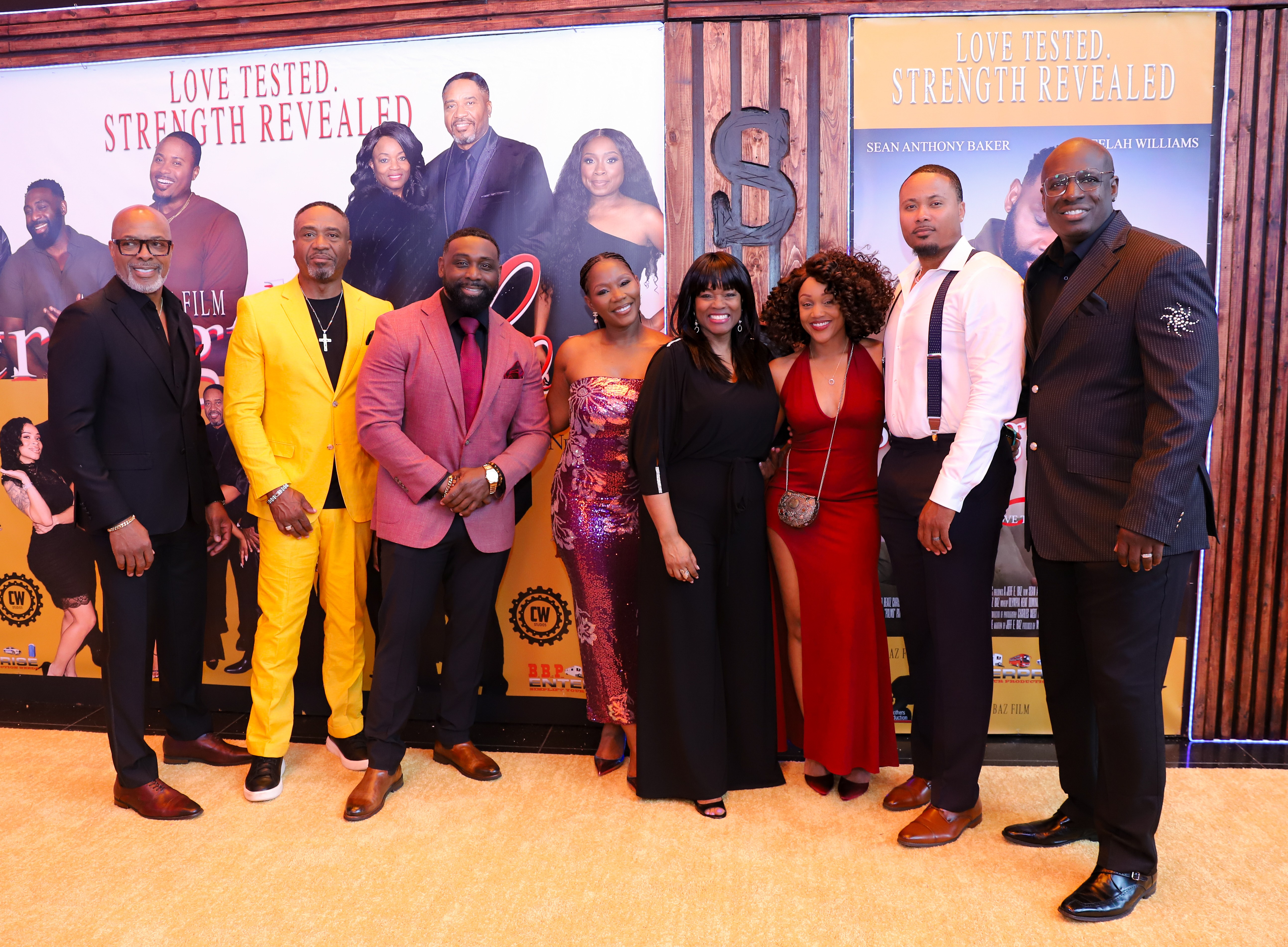Group of ten people standing together indoors, smiling, with promotional posters in the background.