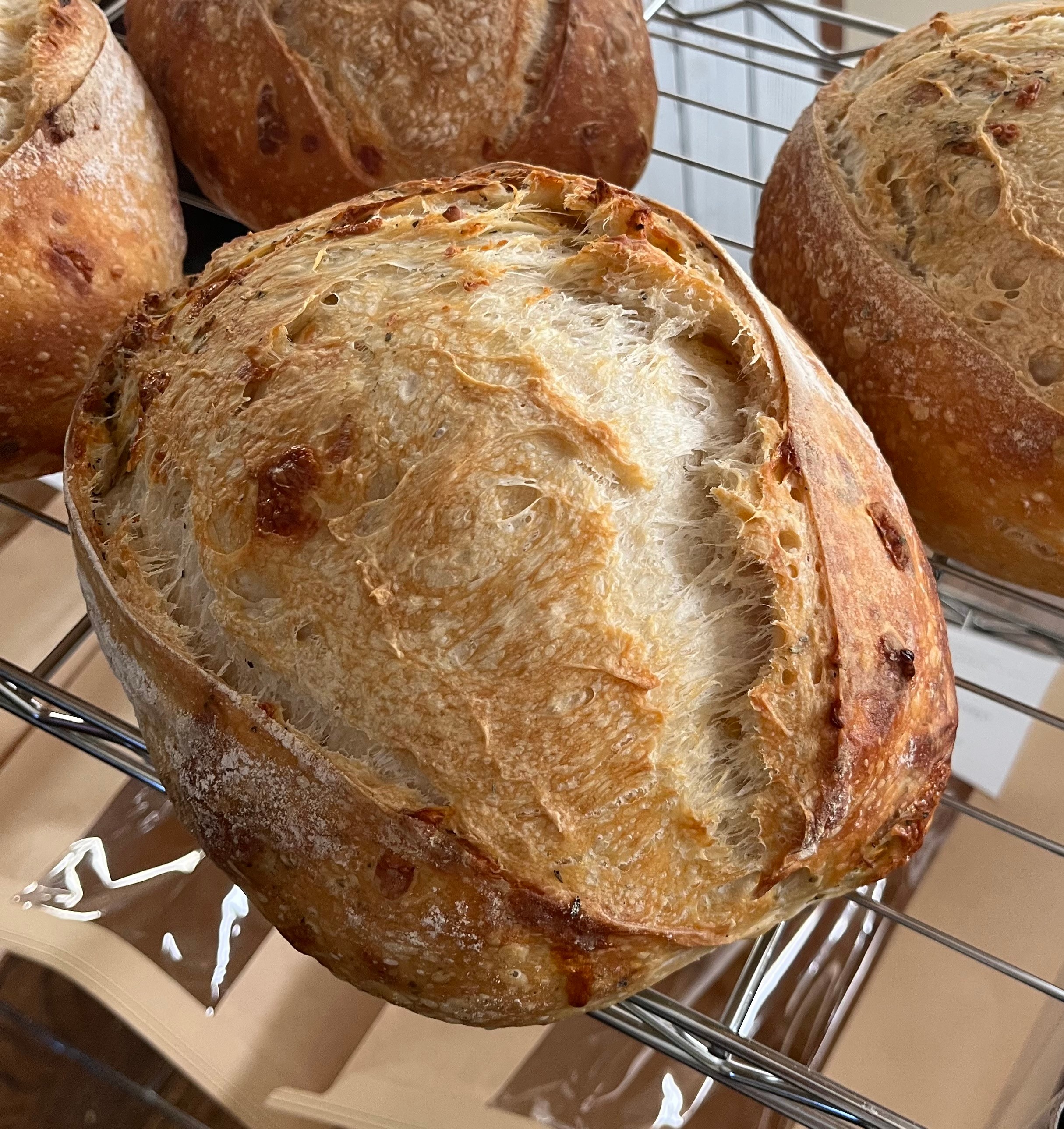 Round, crusty bread with a golden-brown, textured surface on a wire rack.