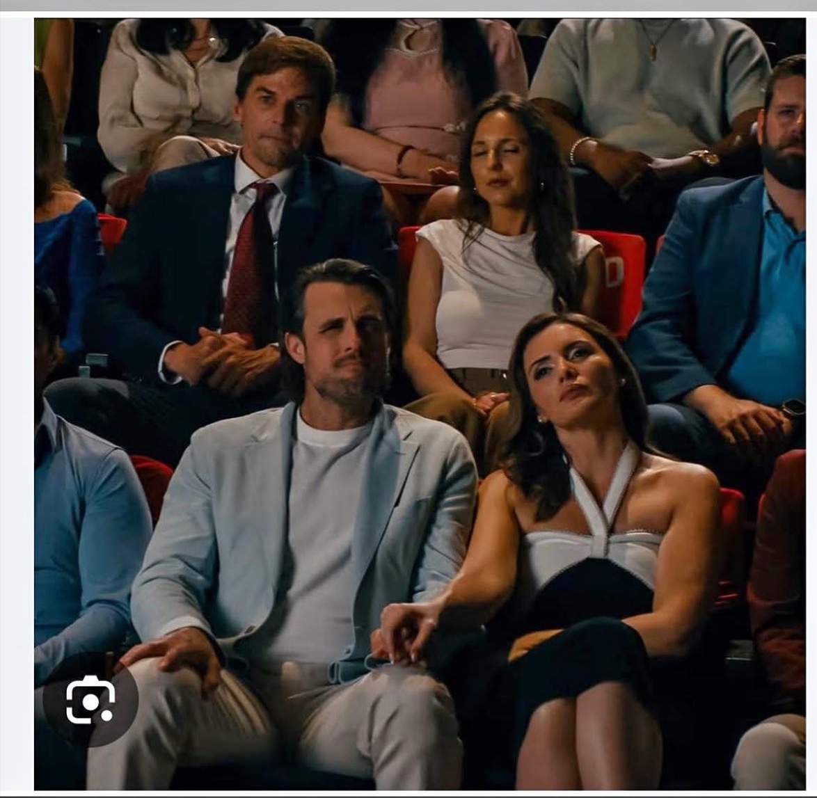 Group of people seated in an auditorium, watching an event, with some looking serious and others attentive.