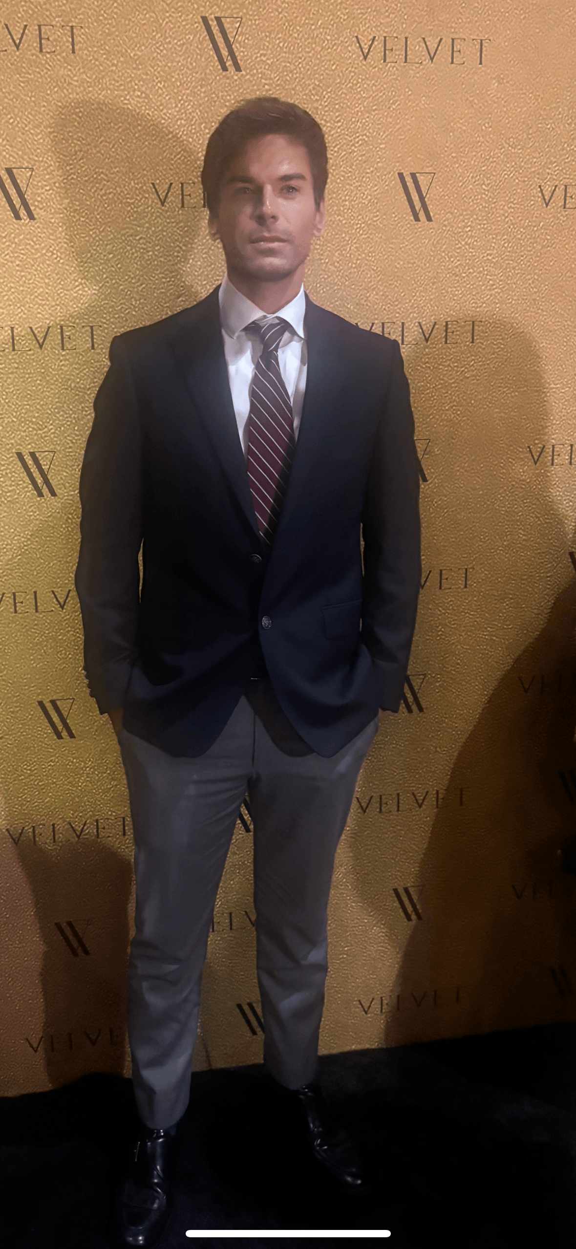 Man in suit and tie standing in front of a yellow backdrop with 'VELVET' written repeatedly.