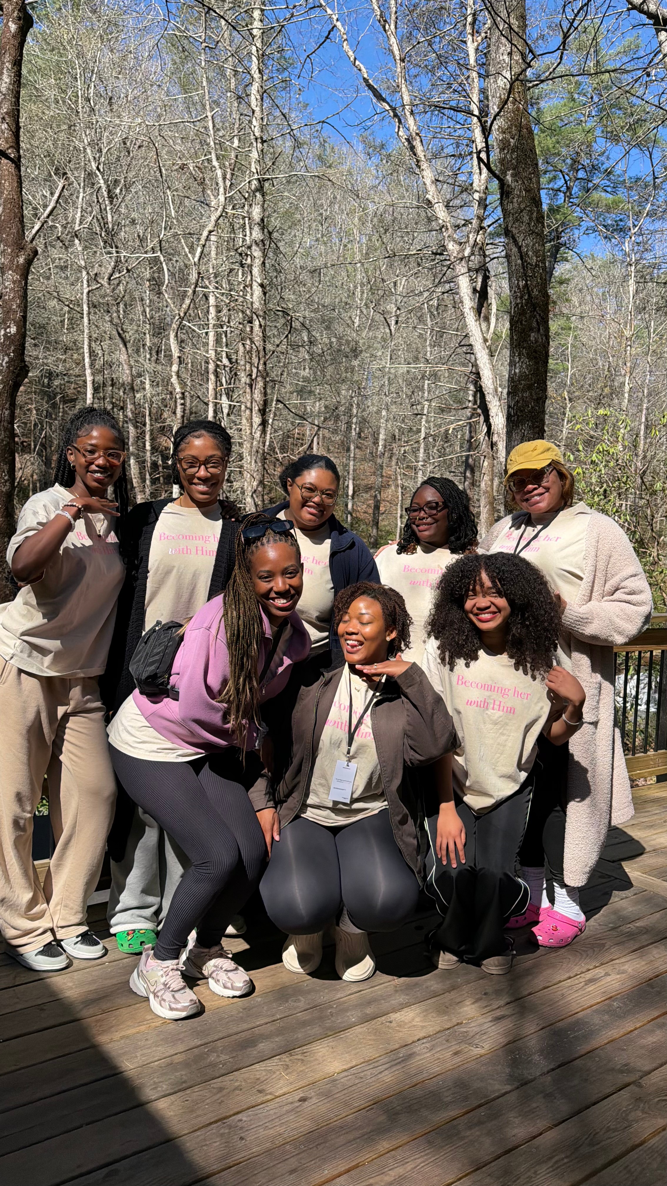 Group of seven people outdoors on a wooden deck, trees in the background, smiling and posing for a photo.