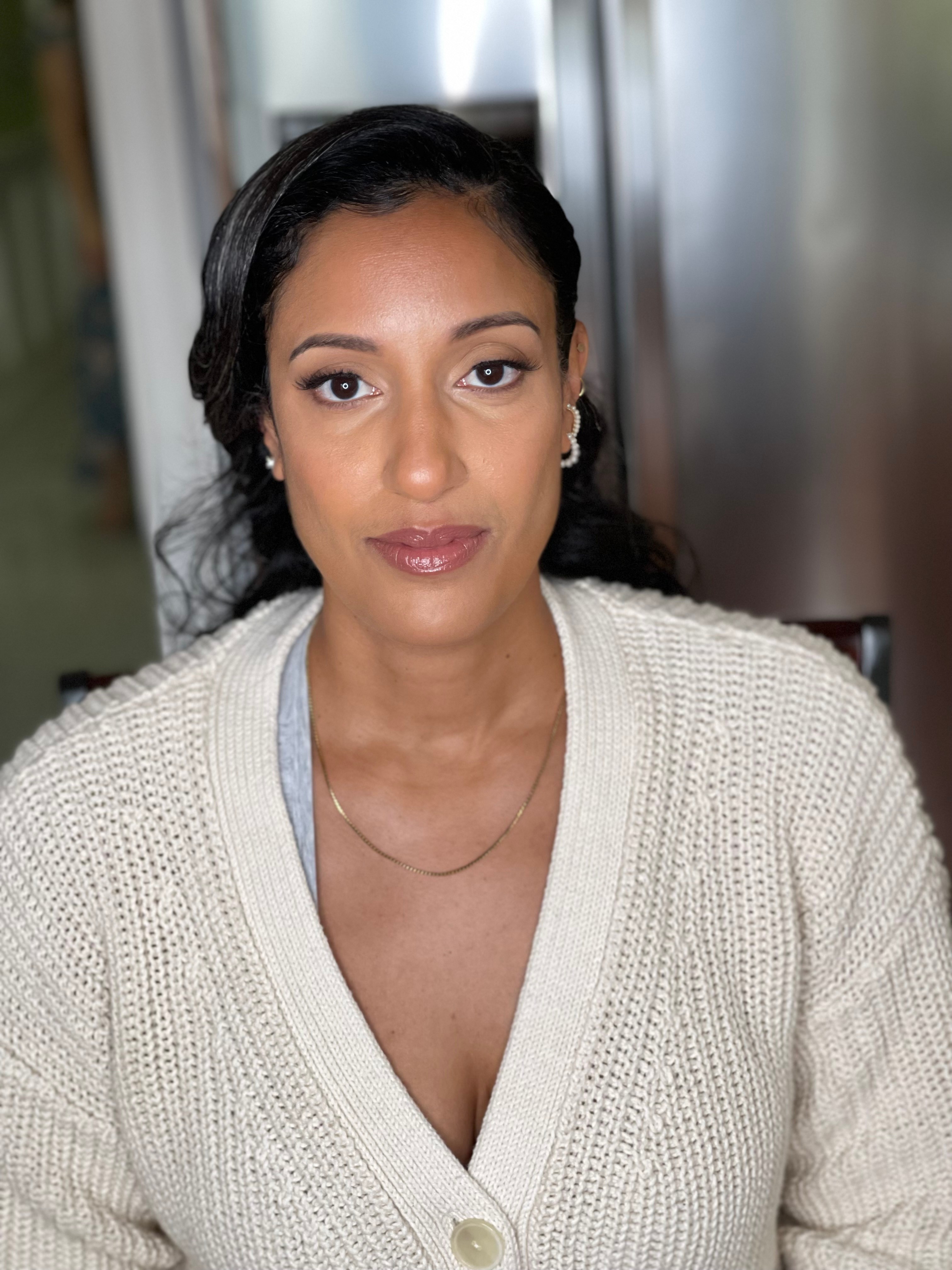 Portrait of a woman with dark hair, wearing a cream-colored sweater, looking directly at the camera.