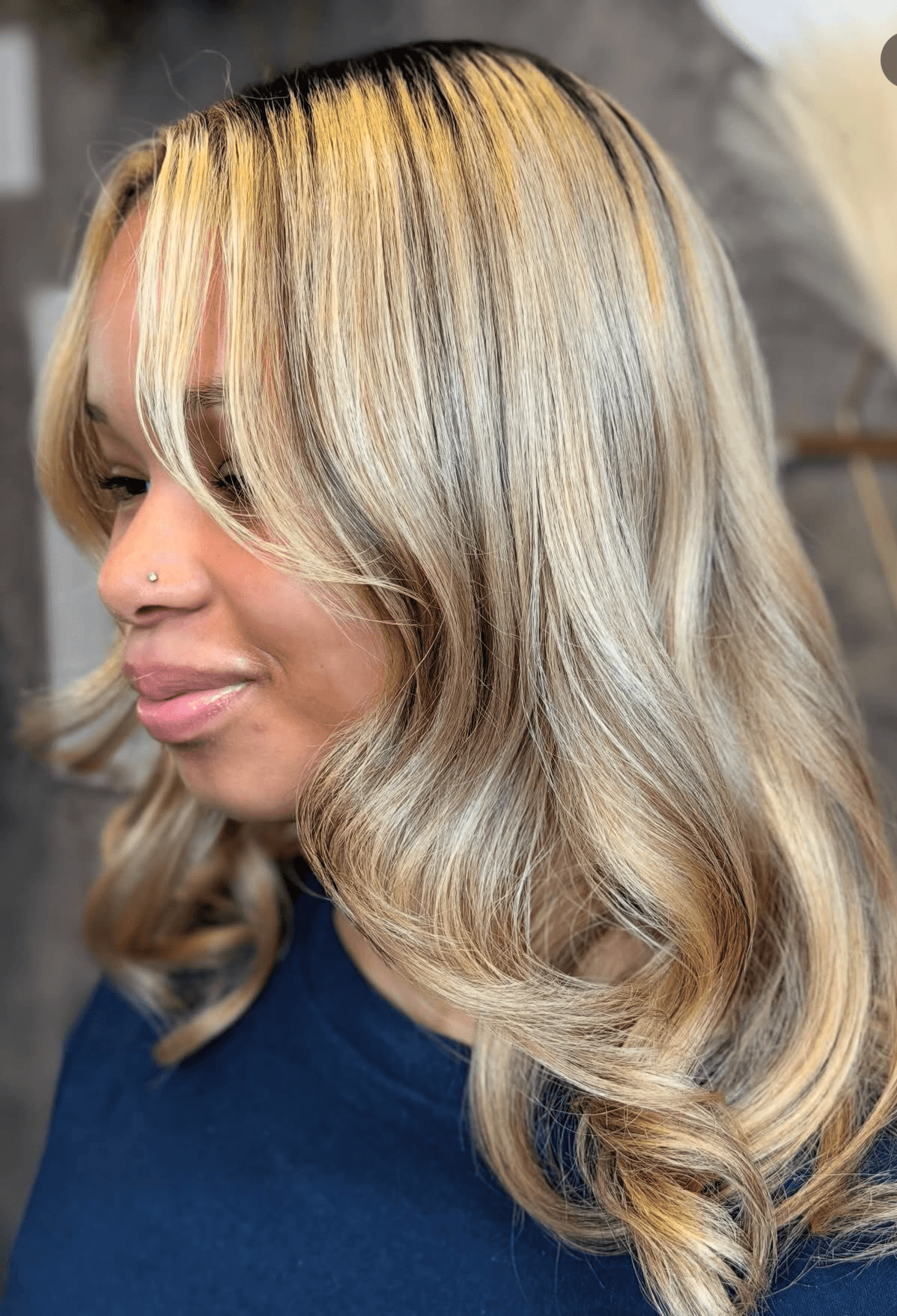 Woman with long, wavy blonde hair and side-swept bangs, wearing a dark top, looking to the side.