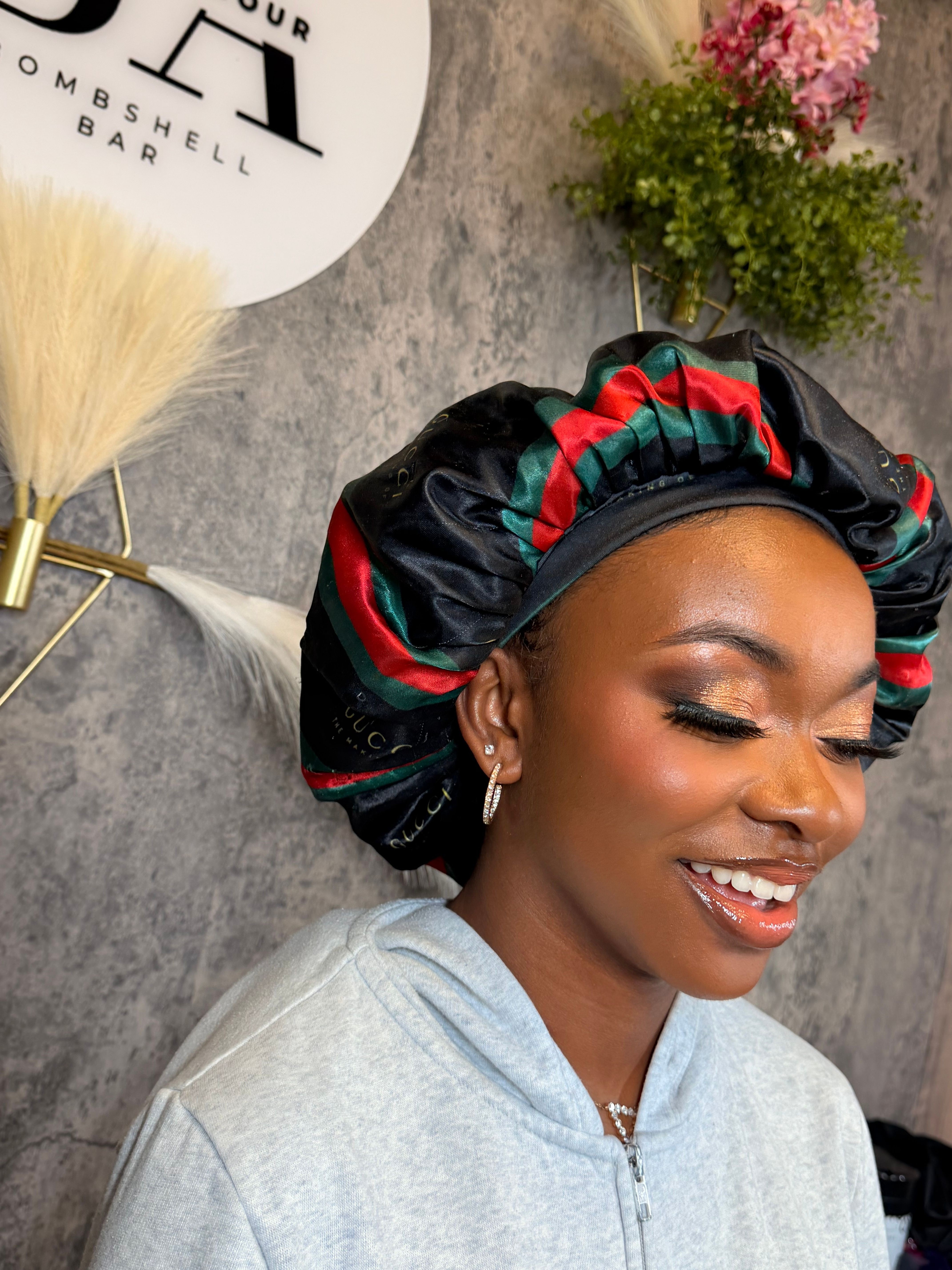 Smiling woman lying on a wooden surface with a colorful headscarf, next to a white plate and a small plant.