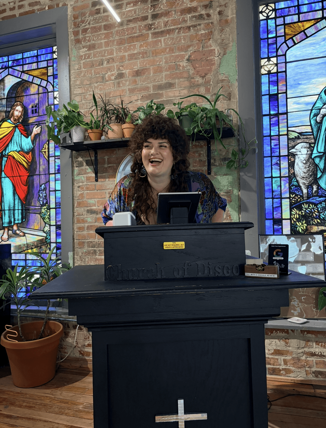Woman with curly hair smiling behind a desk with stained glass windows in the background.