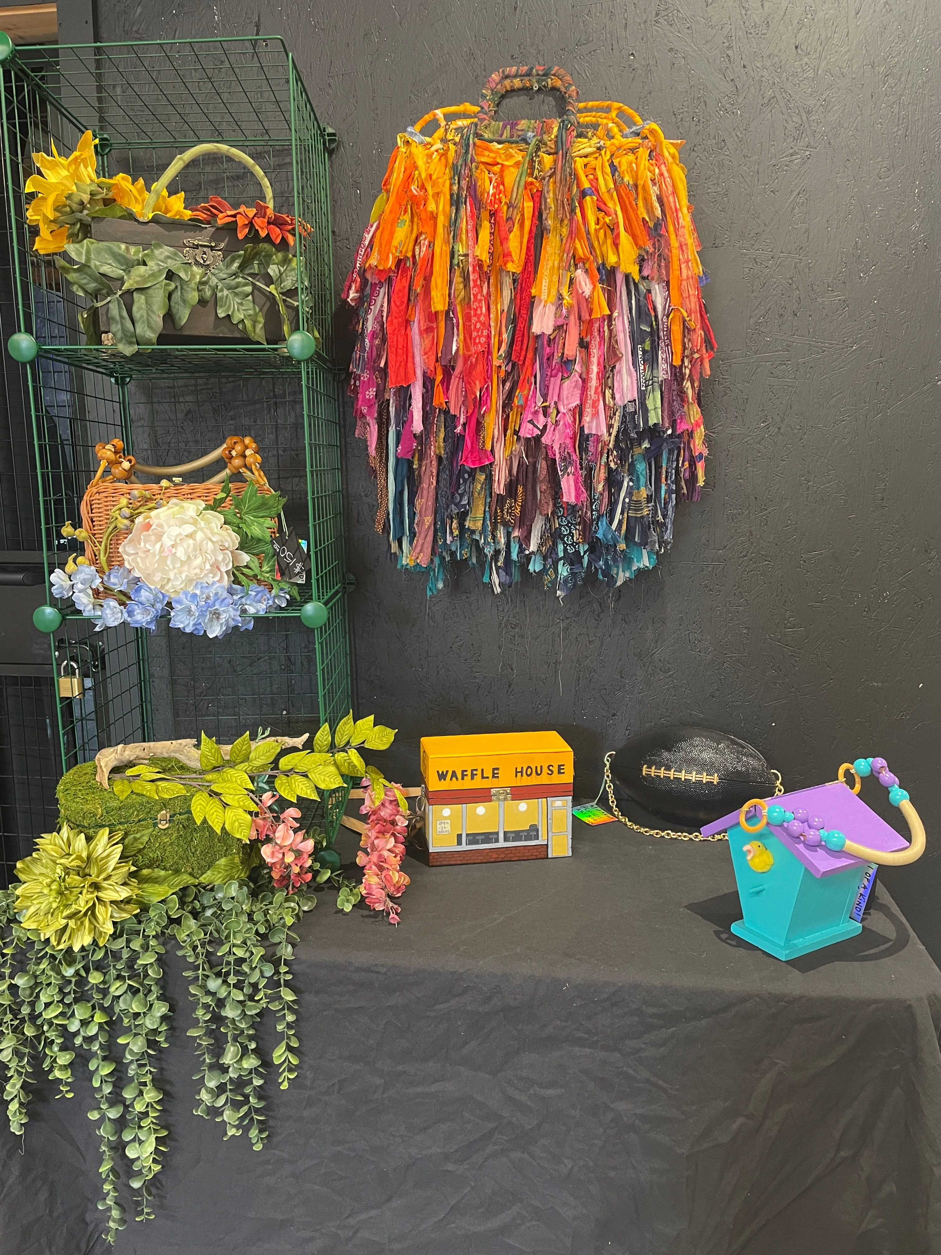 Colorful umbrellas hanging on a green wire, a small yellow flower pot, a pink flower arrangement, and a blue box with a purple handle on a black surface.