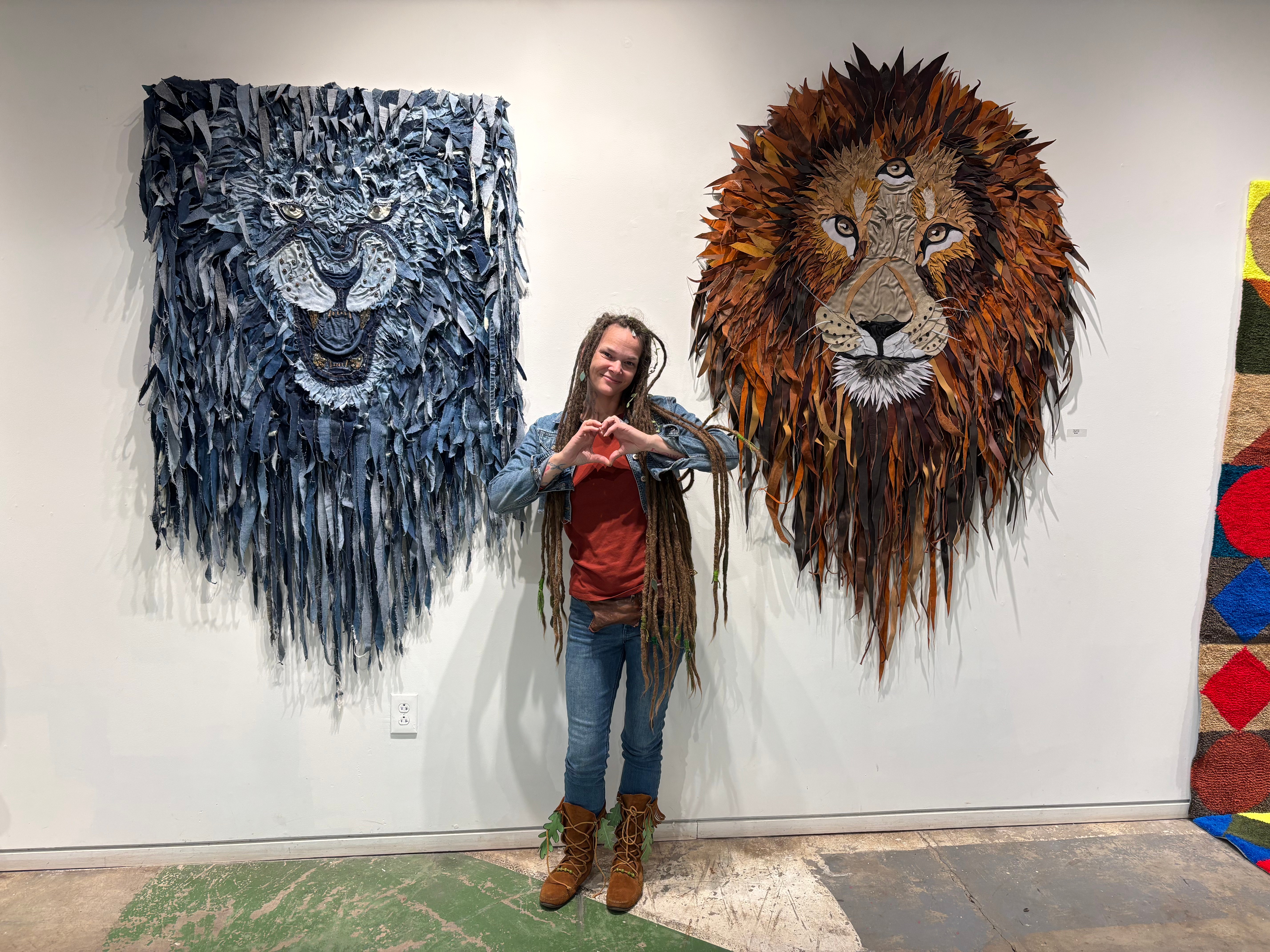 Person standing between two large lion-themed textile art pieces on a white wall, one blue and one brown, in an art gallery.