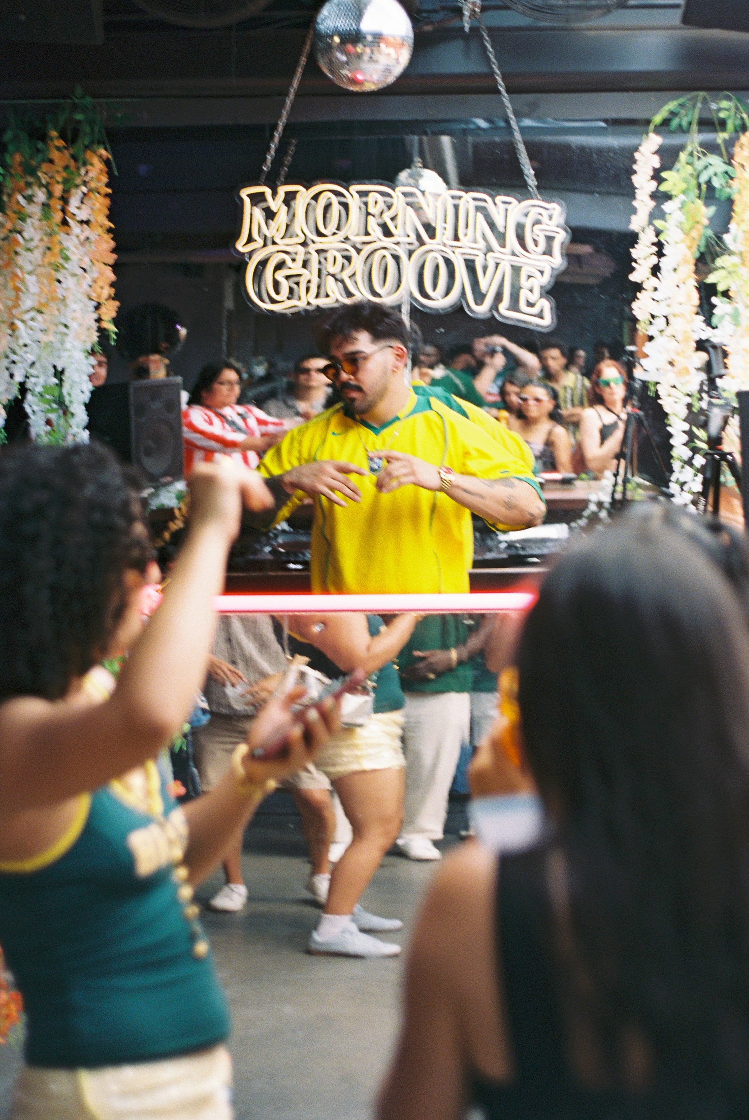 People dancing at a party with a sign reading 'Morning Groove' and floral decorations.