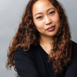 Portrait of a woman with long, curly hair wearing a black top, looking at the camera with a neutral expression.
