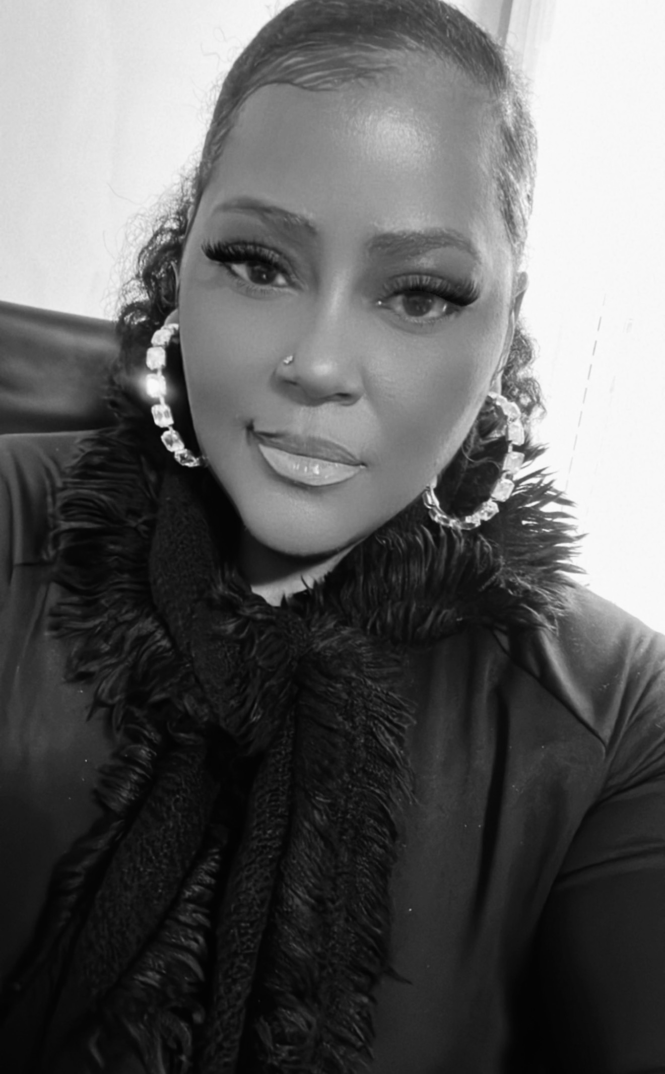 Portrait of a woman with large hoop earrings, wearing a textured scarf and a jacket, smiling slightly.