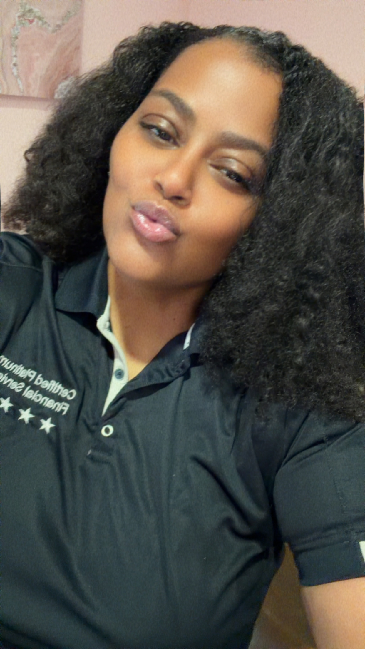 Woman with curly hair making a kiss face, wearing a dark polo shirt, in an indoor setting.