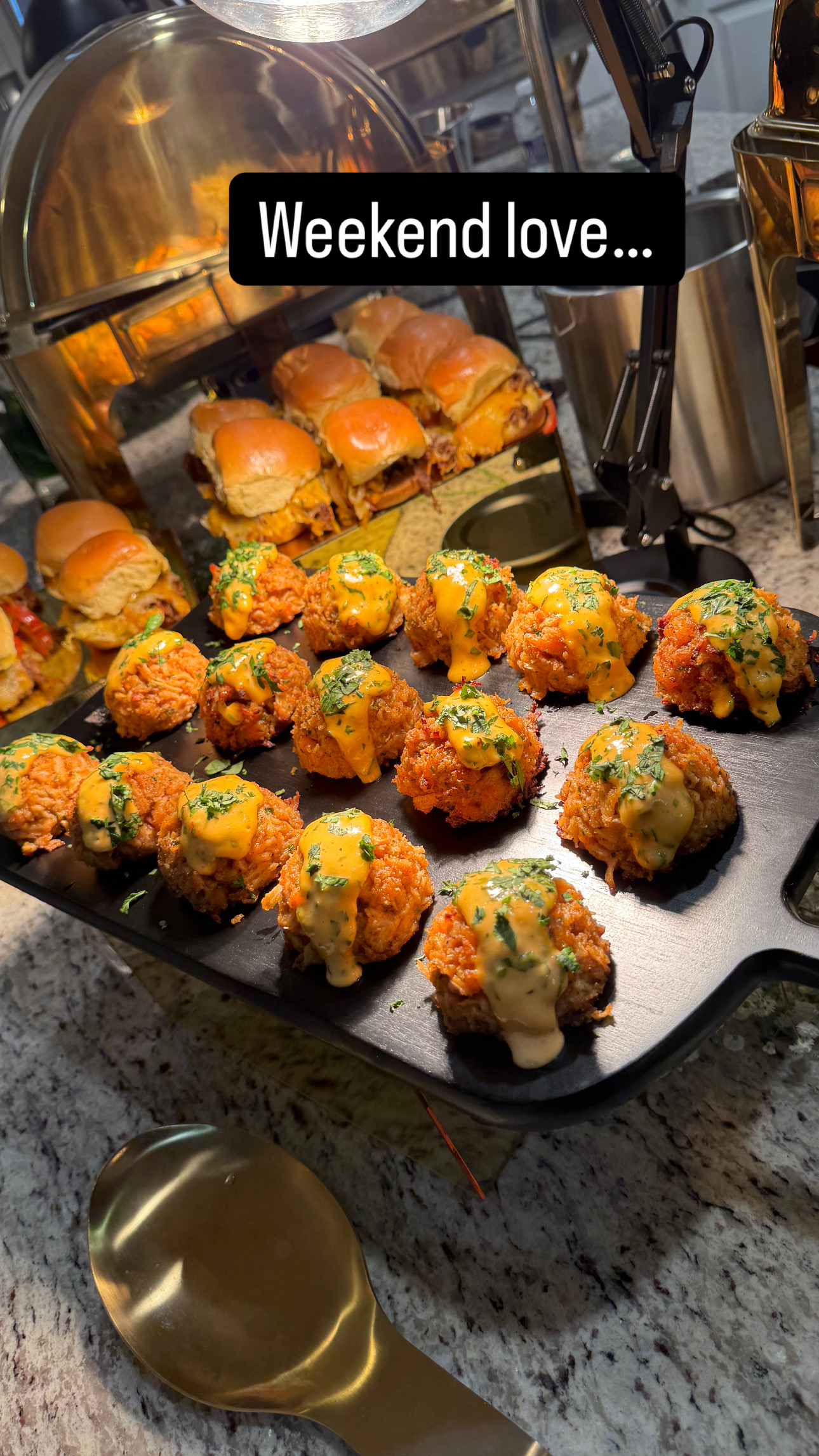 Tray of assorted fried appetizers on a kitchen counter with a spoon nearby, with a sign reading 'Weekend love...'.
