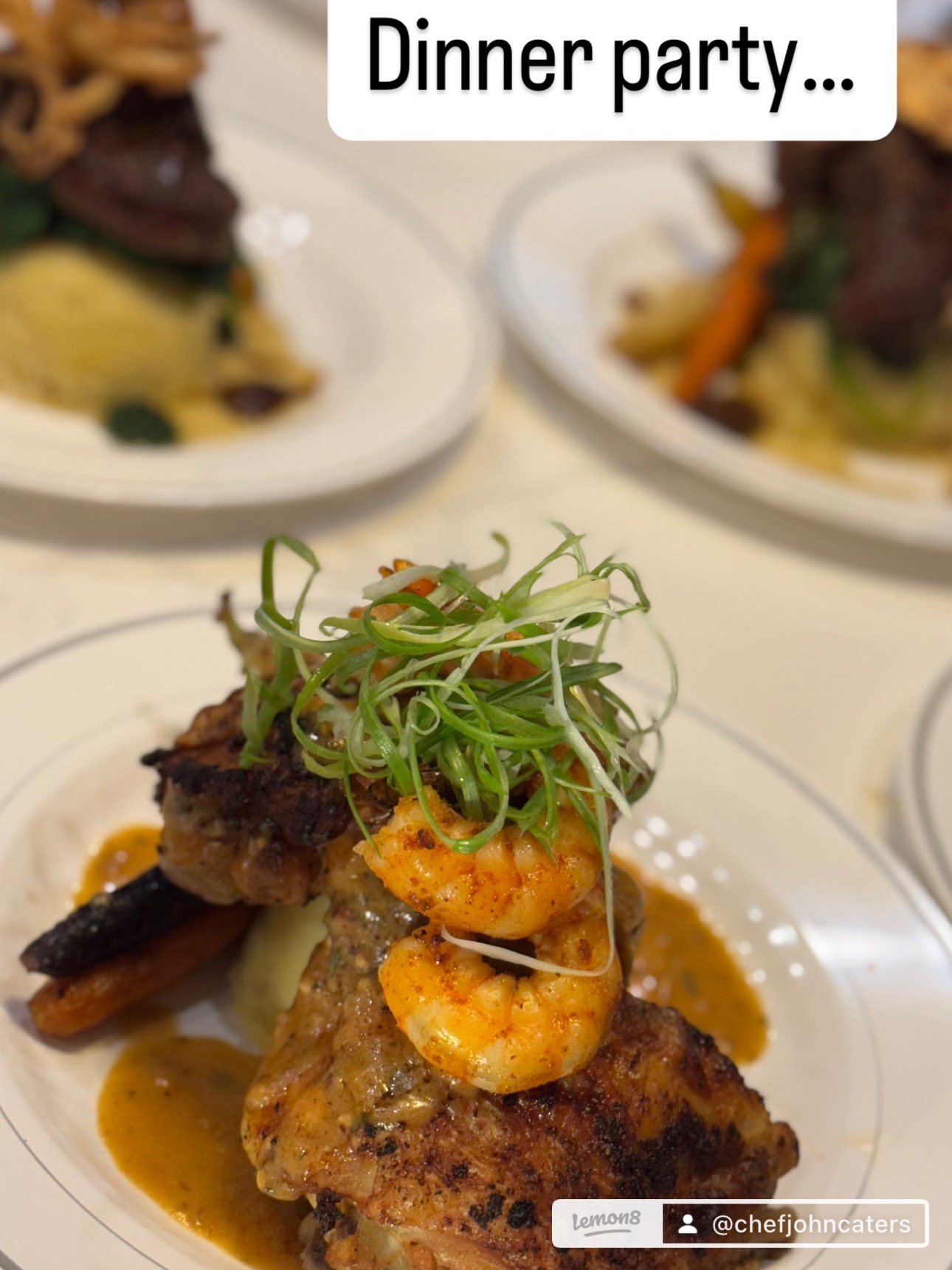 Plate with grilled meat, shrimp, and vegetables, garnished with greens, at dinner party, with other plates in background.