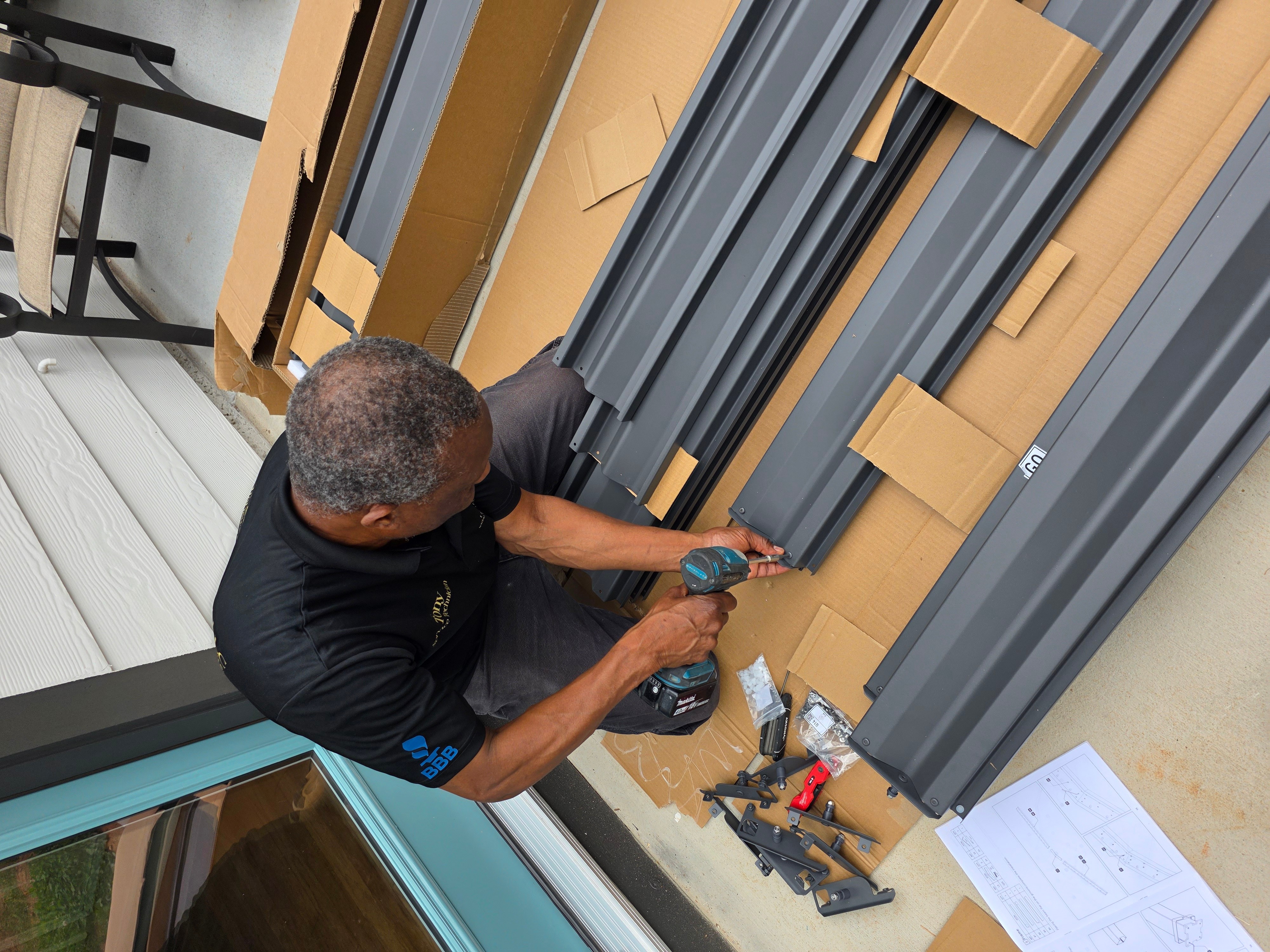 Person working with tools on metal and cardboard materials, with a paper and tools nearby, viewed from above.