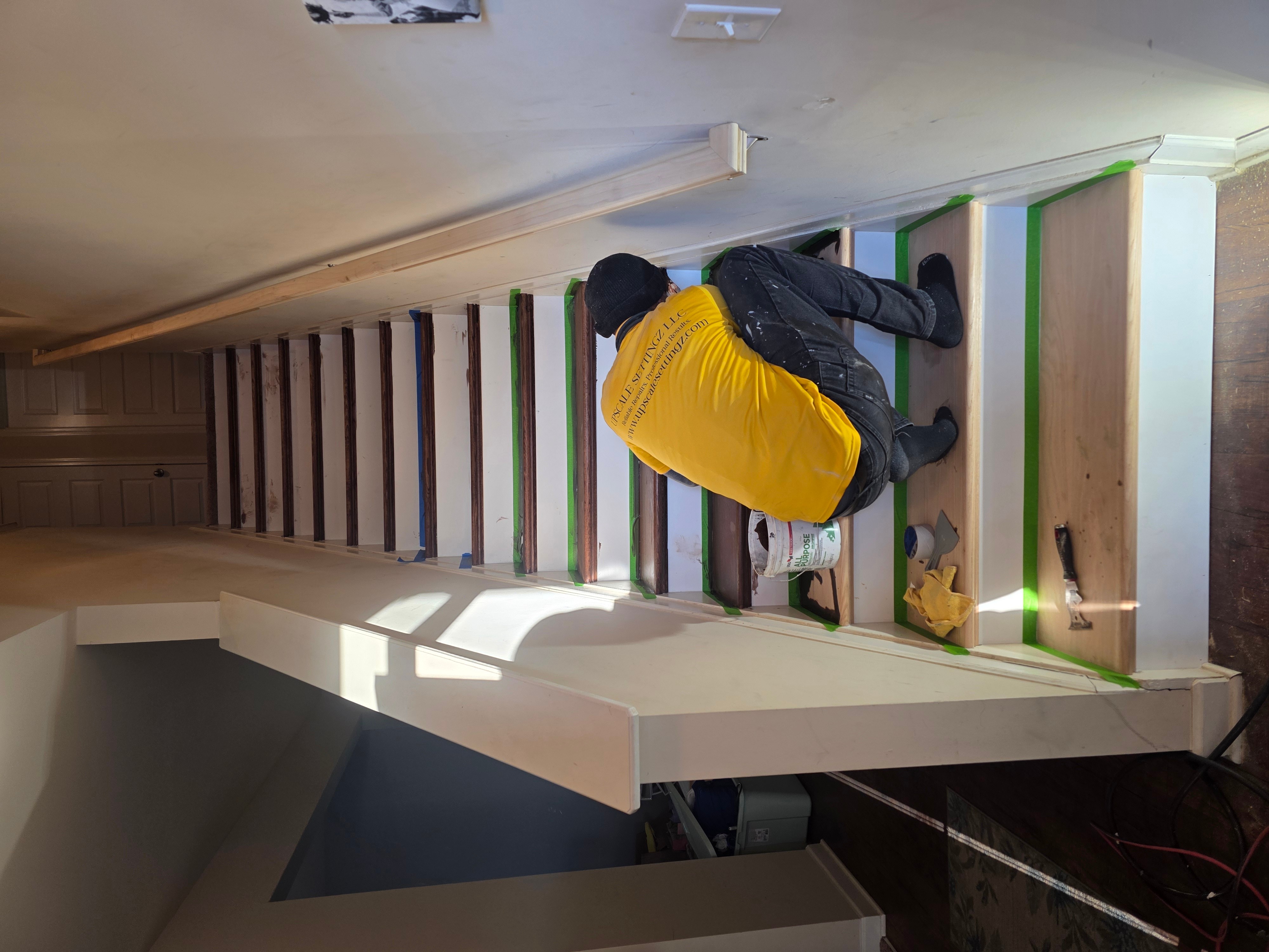 Person crouching on stairs, wearing a yellow shirt and black jacket, with a small dog nearby, in an indoor setting.