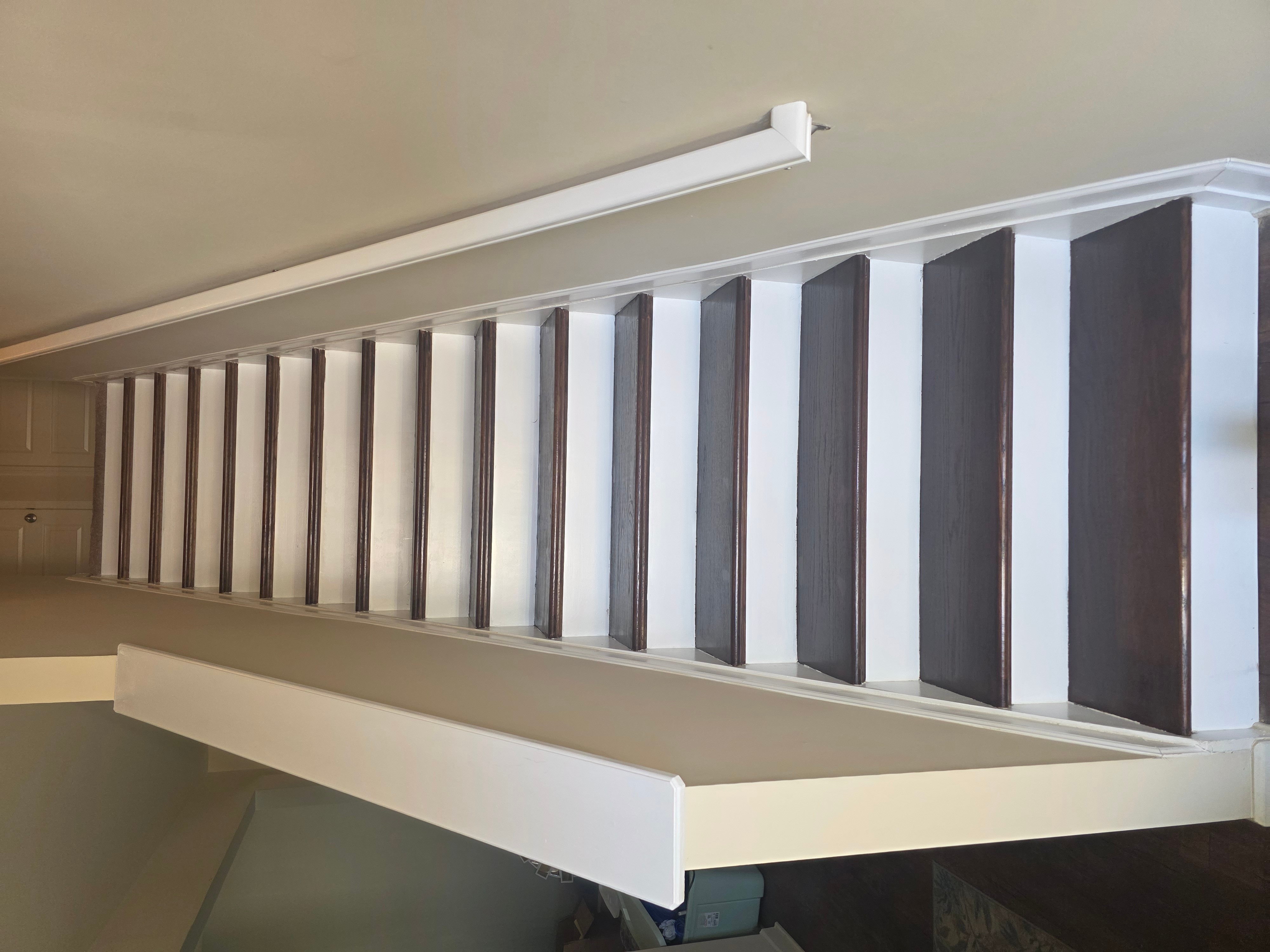 Staircase with dark treads and white risers viewed from above, with a white wall on the side.