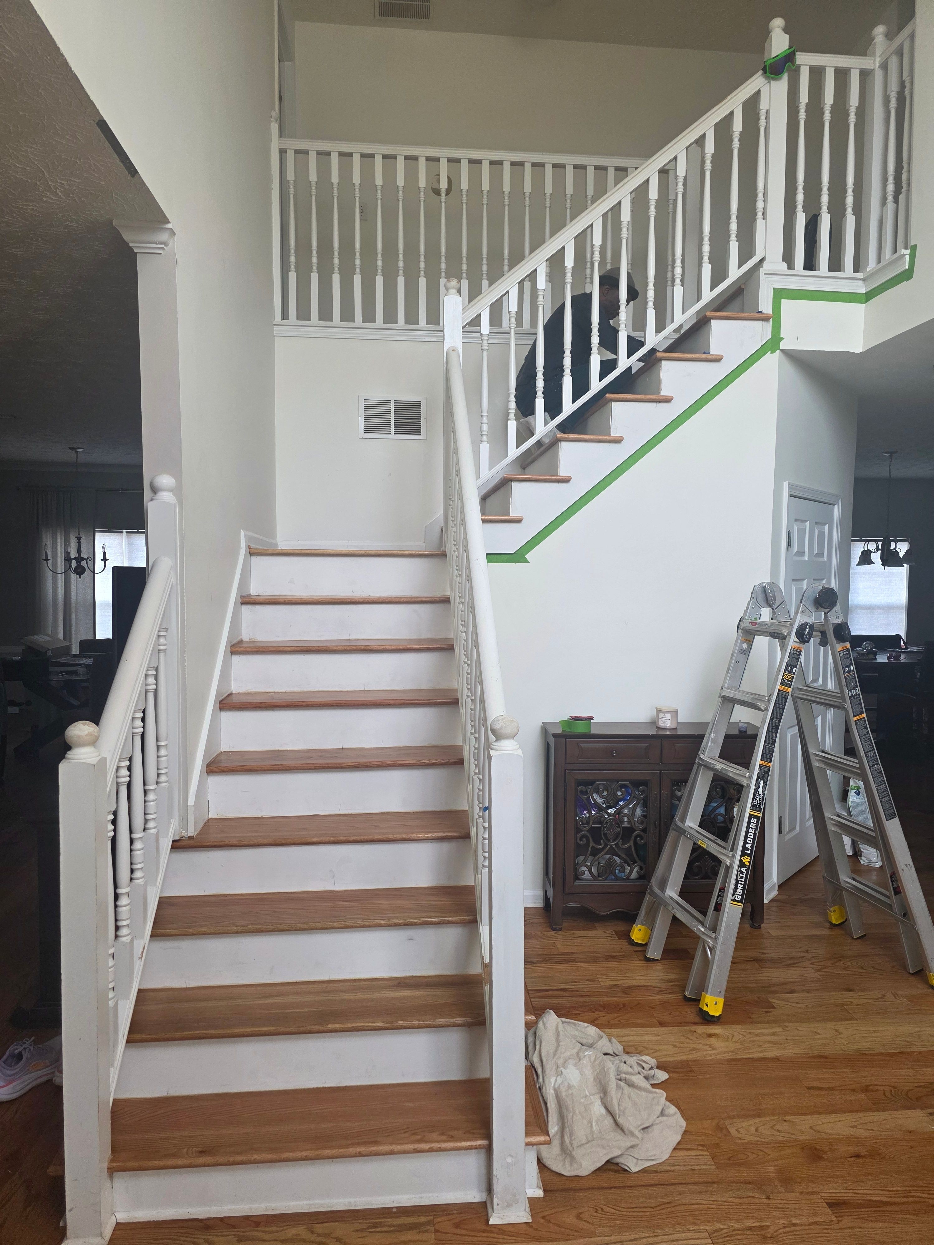 Staircase with wooden steps and white railing leading to upper floor, with ladder and tools nearby, and a bag on the floor.