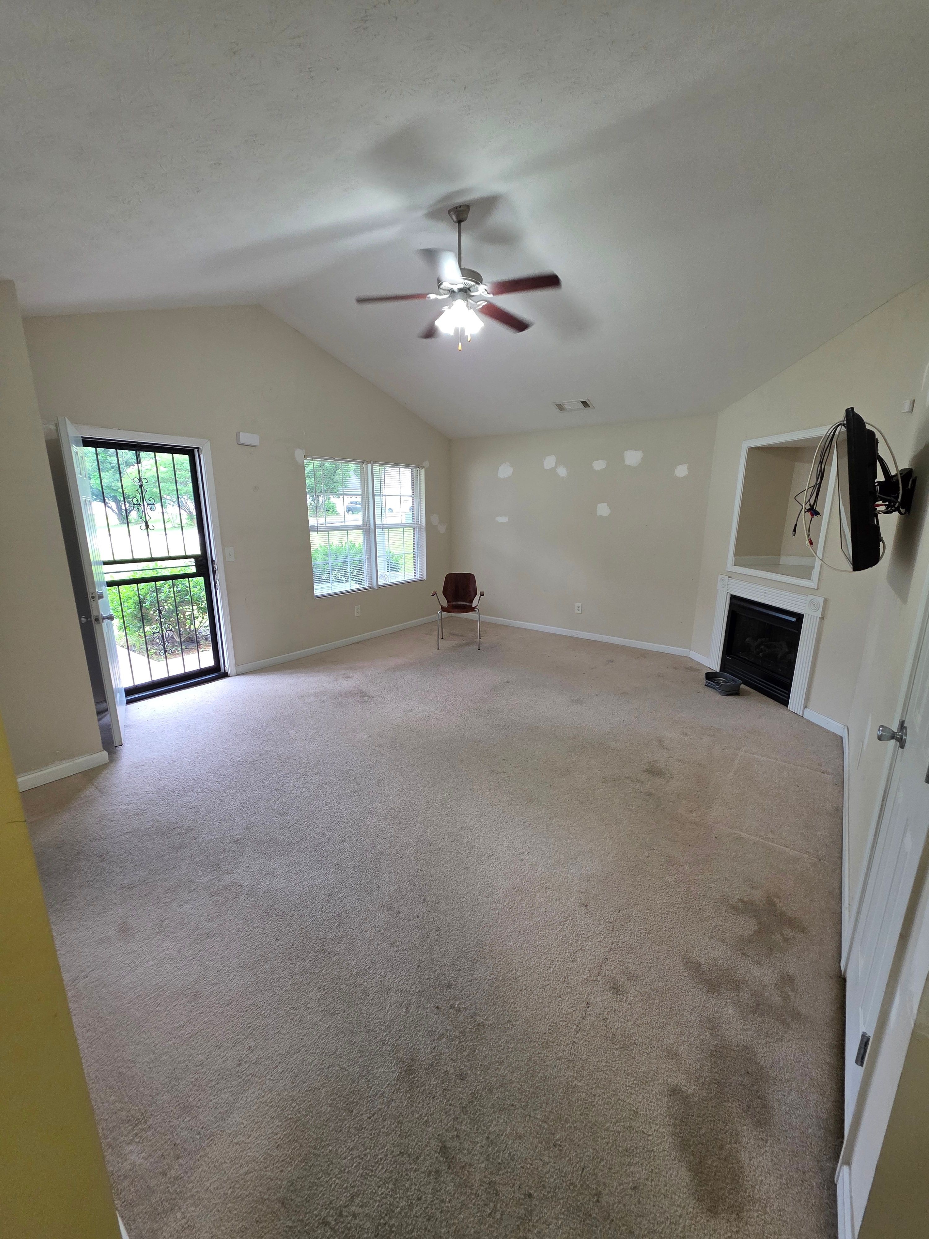 Empty room with beige carpet, white walls, ceiling fan, window, and sliding door leading outside.