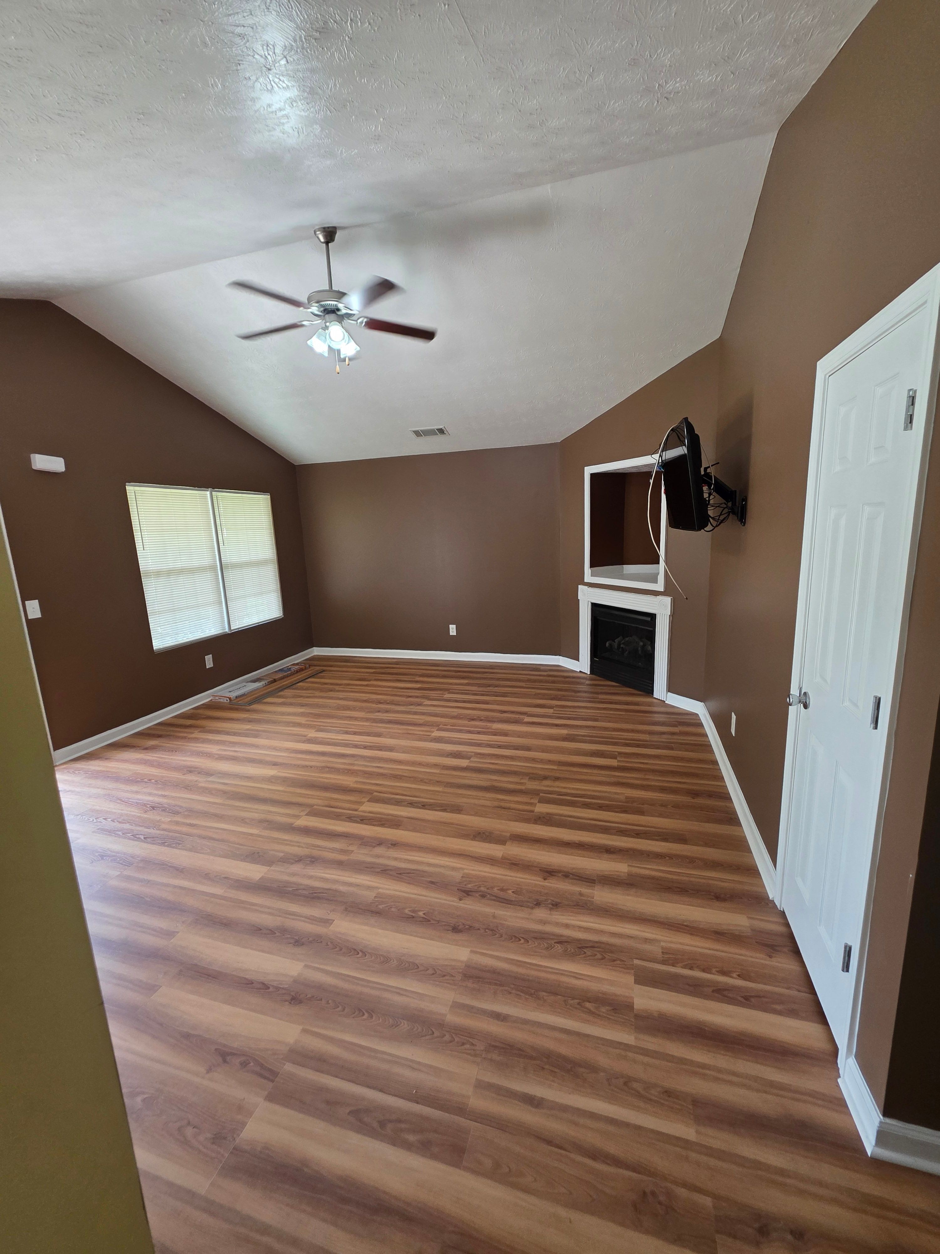 Room with hardwood floor, window, ceiling fan, and door, viewed from an angle.