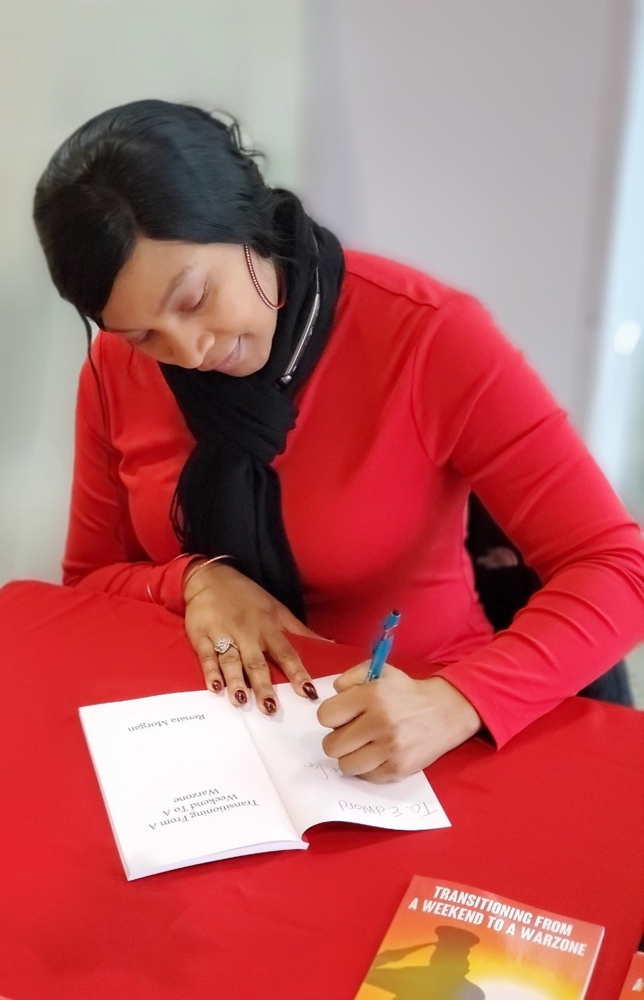 Woman in red shirt writing in a notebook with a pen, sitting at a table.