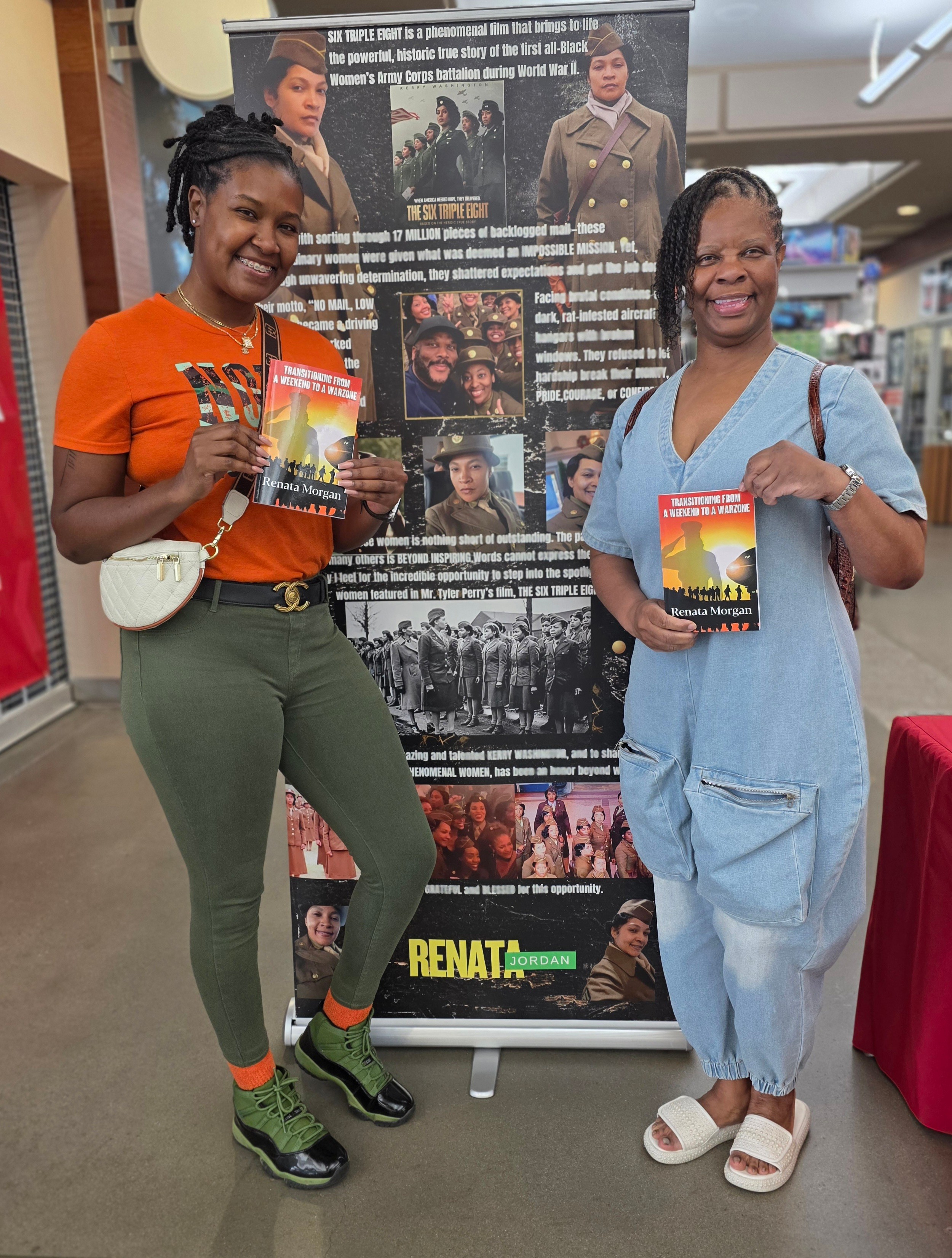 Two women stand in front of a large informational poster, smiling and holding books, inside a bookstore or library.