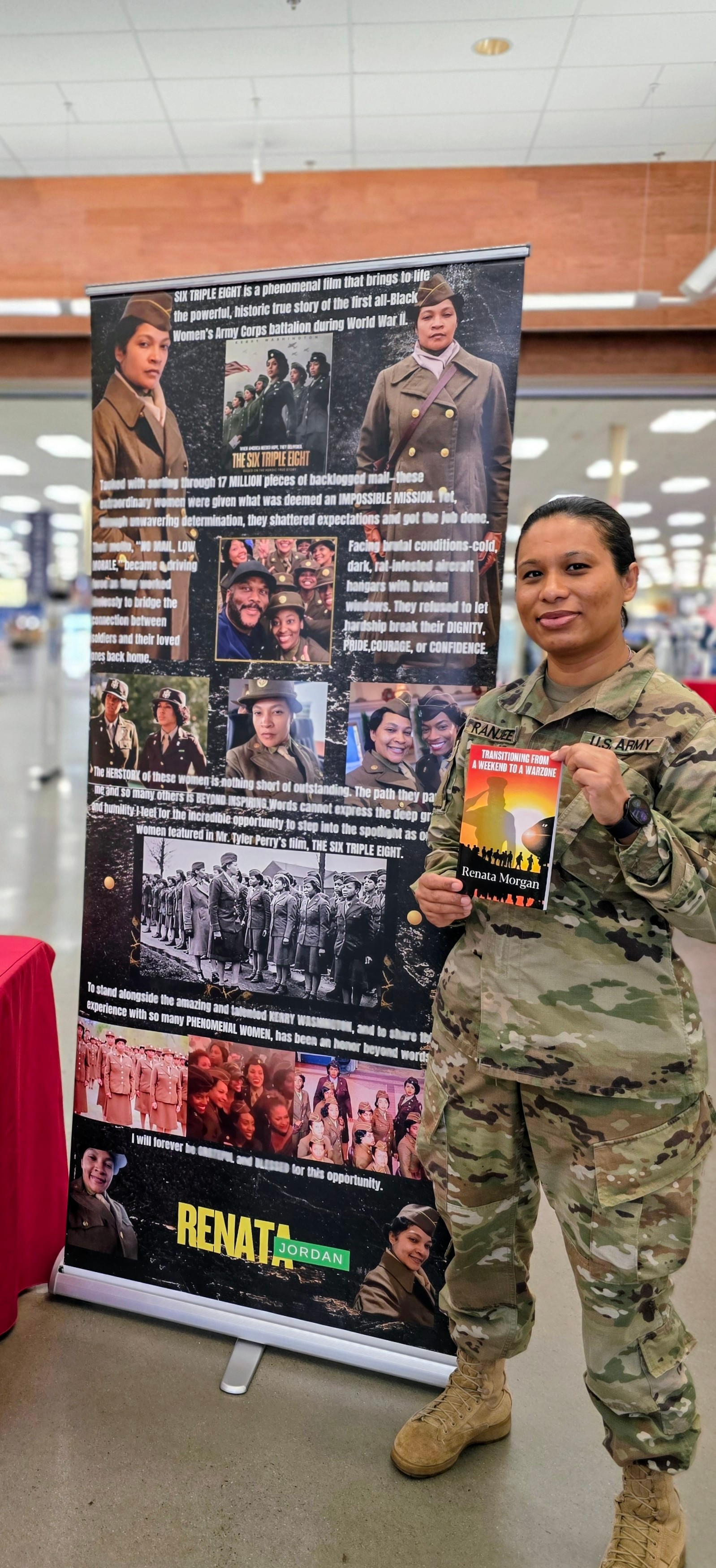 Woman in military uniform holding a book, standing next to a large informational poster, in an indoor setting.