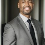 Man in gray suit and tie smiling in a professional setting.