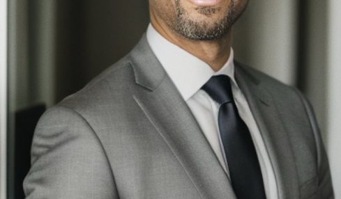 Man in gray suit and tie smiling in a professional setting.