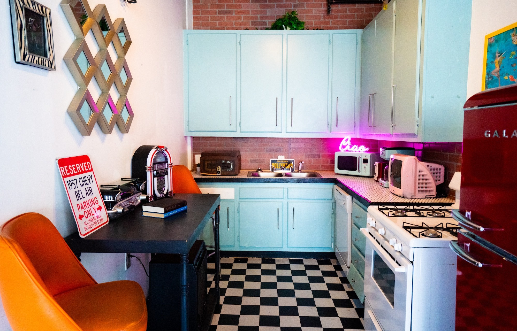 Kitchen with light blue cabinets, black and white checkered floor, orange chairs, and various appliances, including microwave and coffee maker.