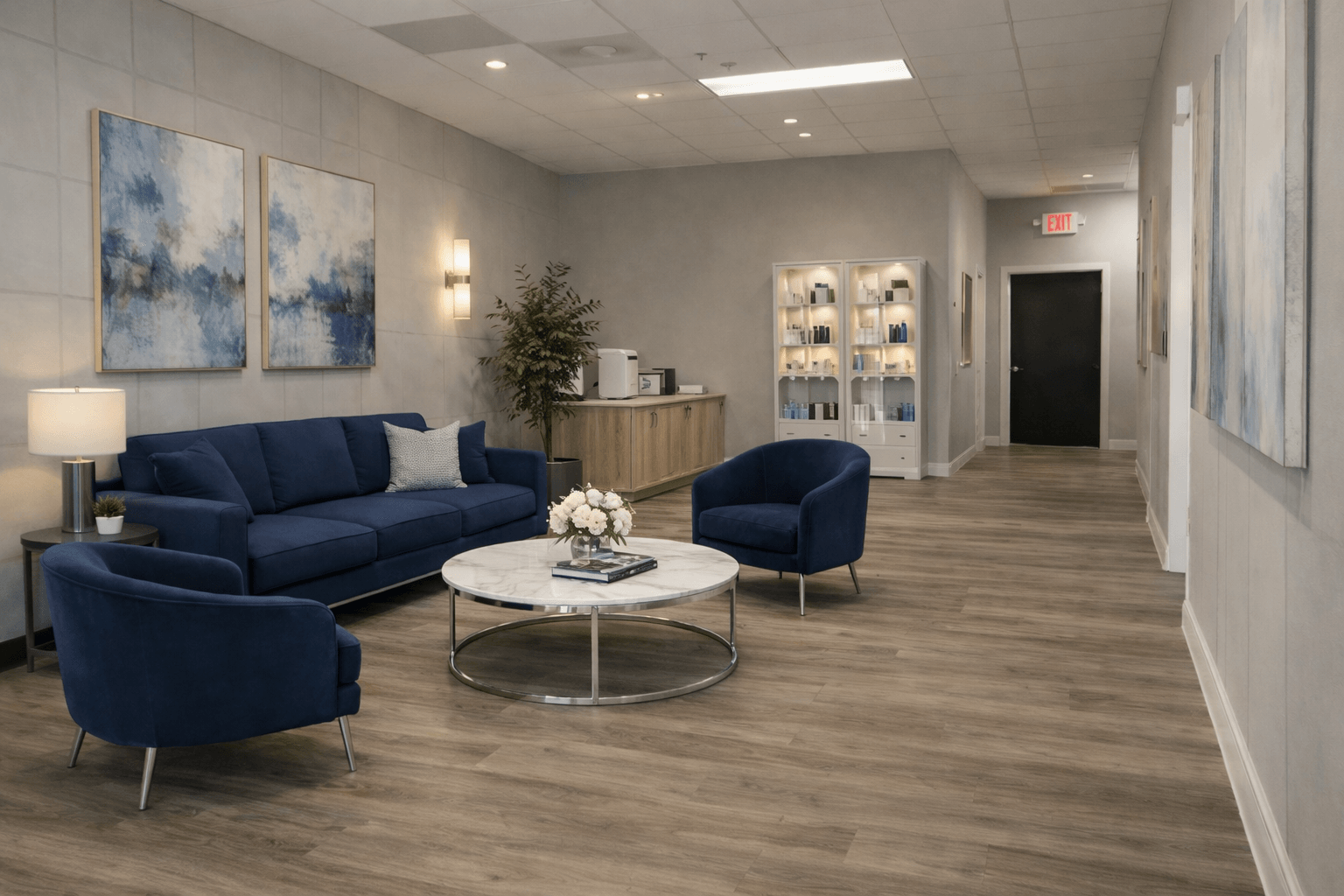 Lobby with blue sofa, armchairs, round coffee table, artwork, and a small bar area, with wood flooring and neutral walls.