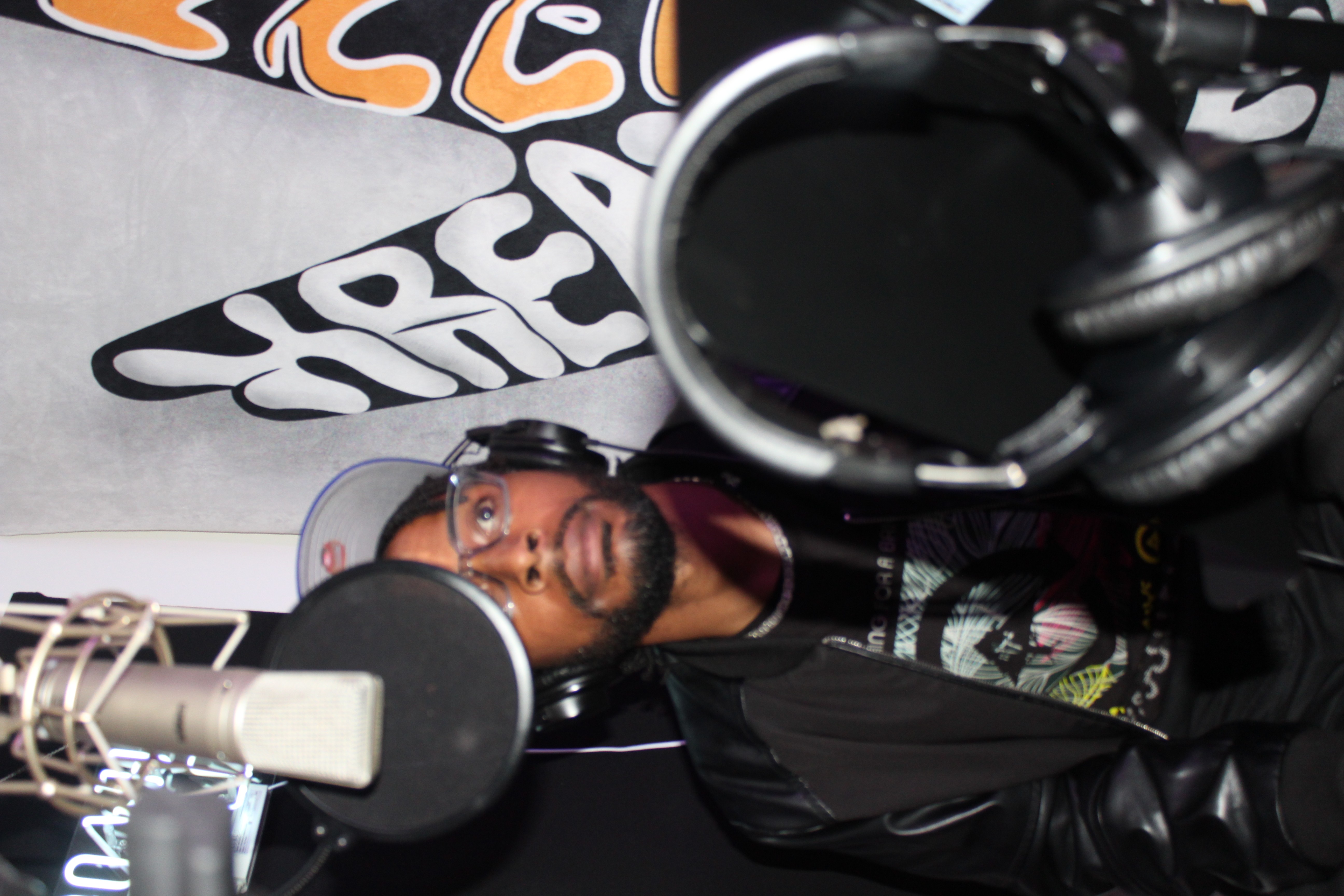 Person lying in a recording studio with headphones, microphone, and soundproofing, looking at the camera.