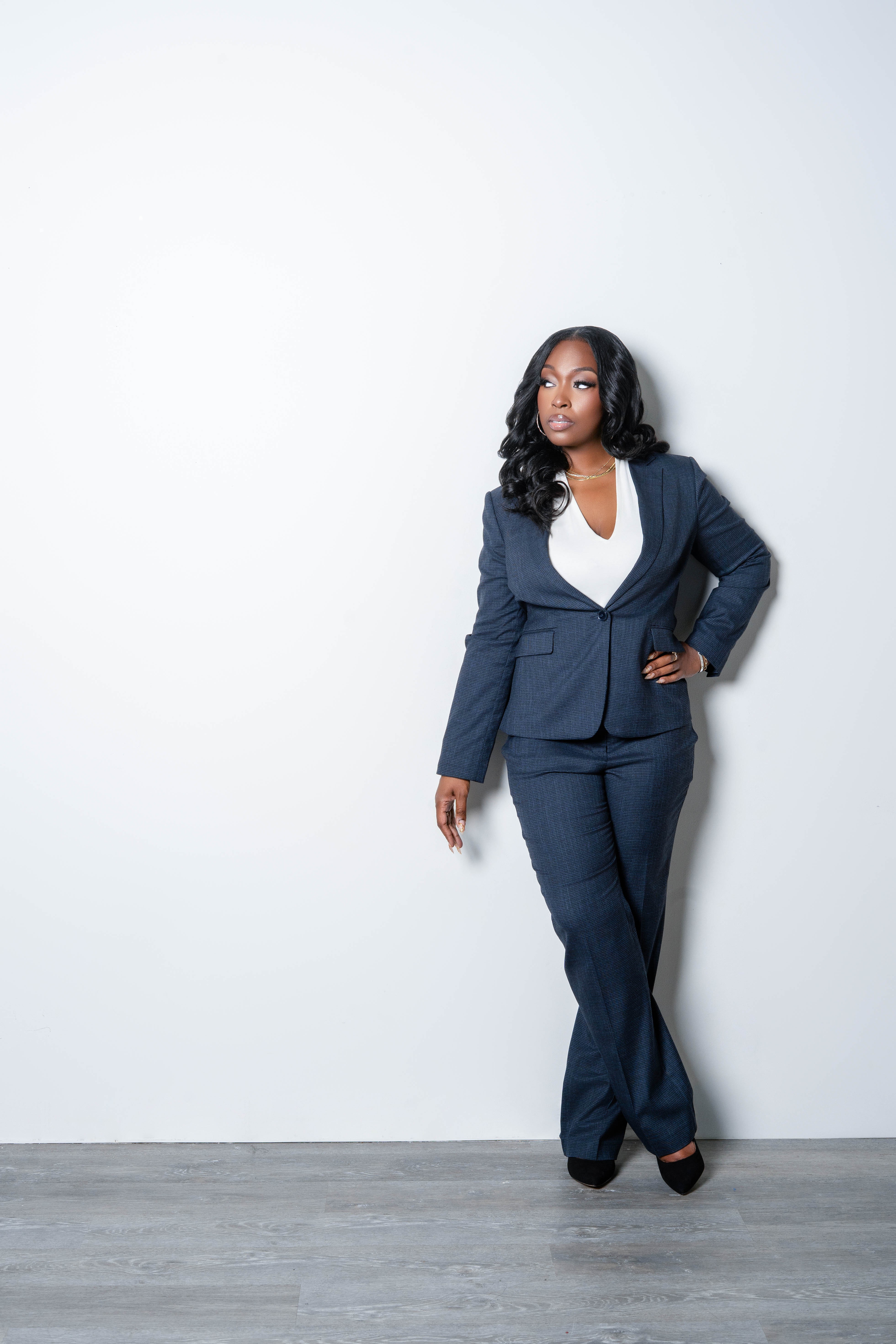 Woman in a navy suit standing with hand on hip against plain white background.