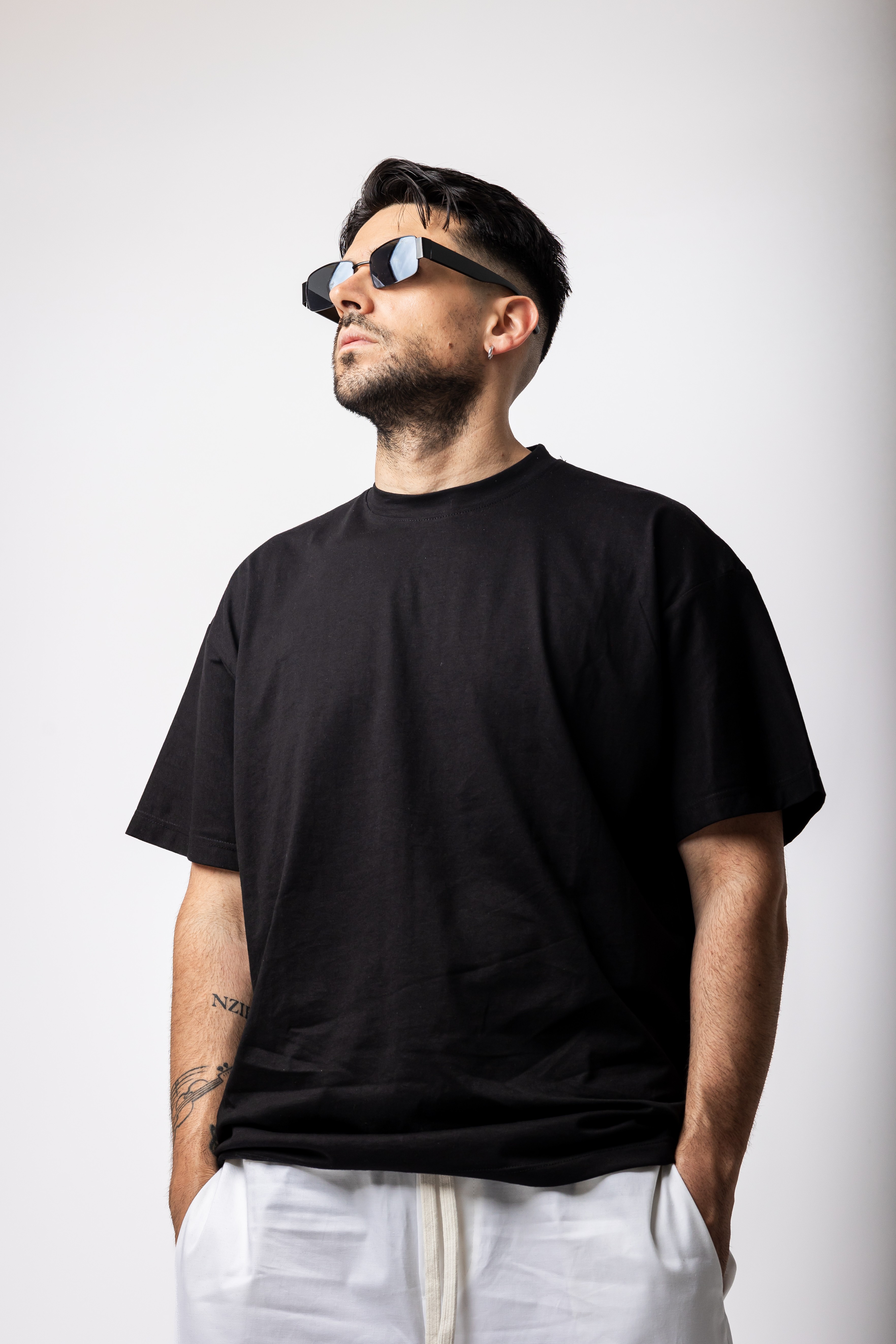 Man wearing sunglasses and a black t-shirt, standing against a plain background.