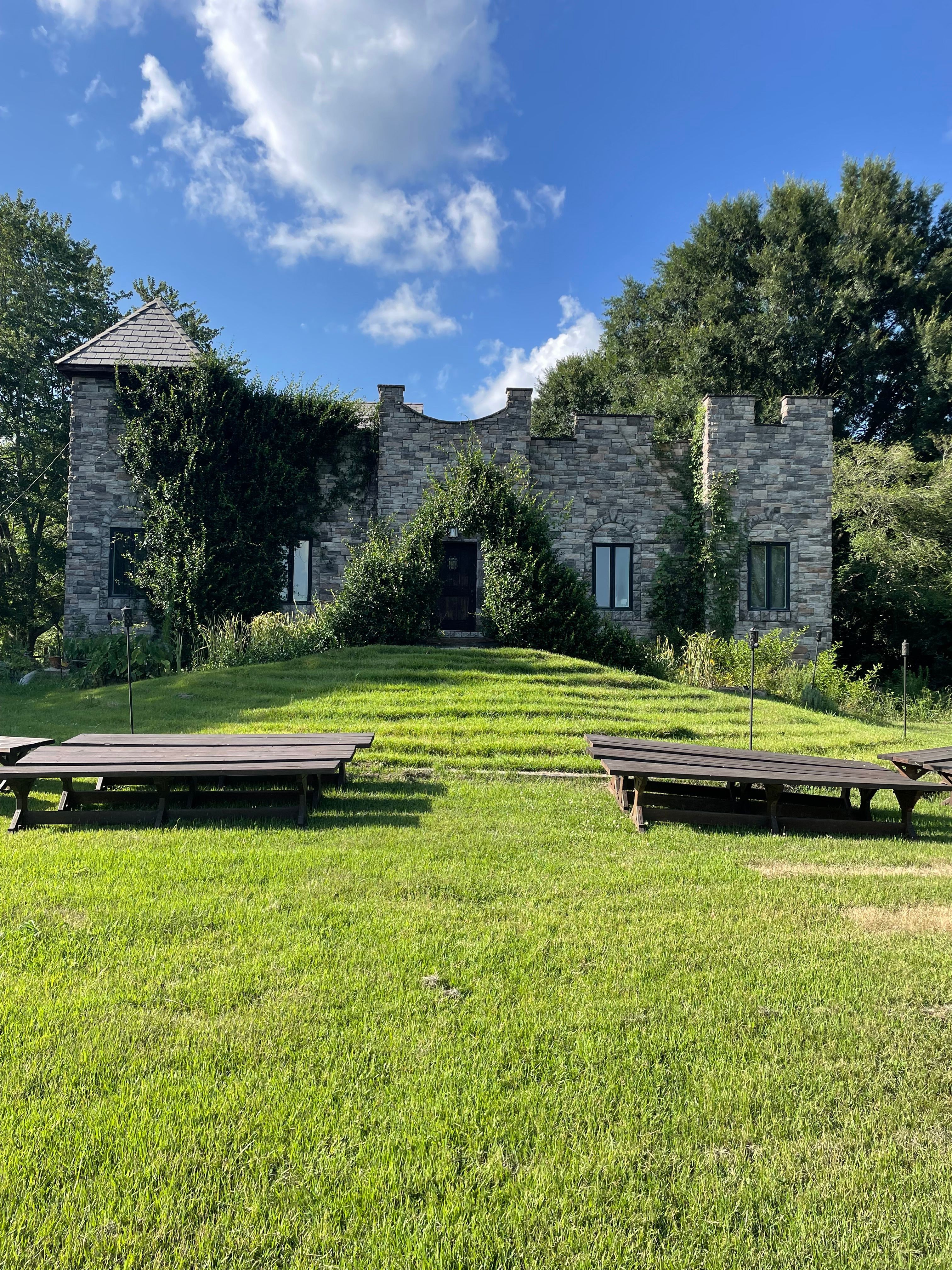 Stone building with trees and a grassy lawn under a blue sky with clouds.
