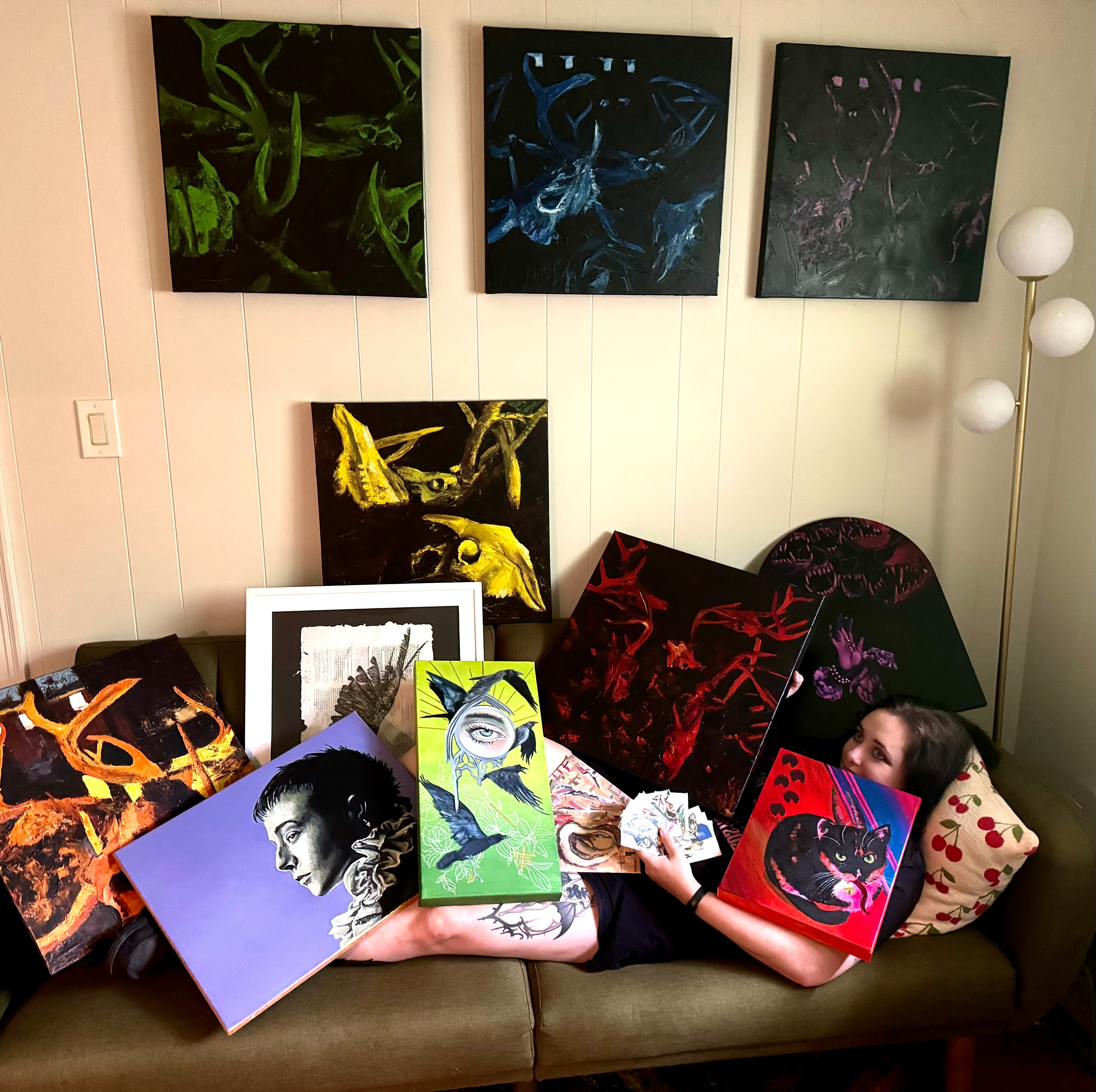 Person lying on a couch holding colorful books, surrounded by artwork and a pillow with polka dots.