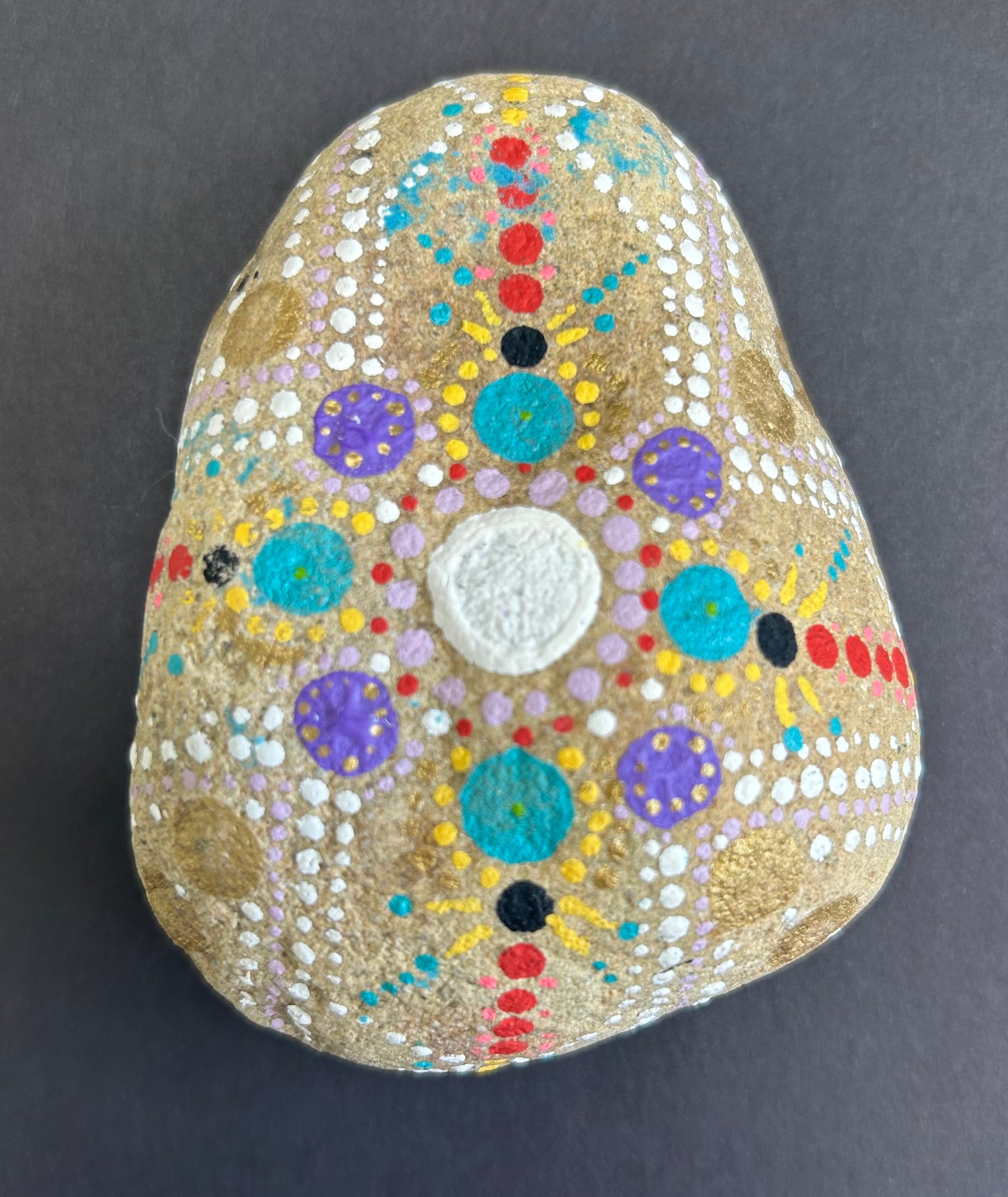 Decorative stone painted with colorful dots and patterns on a dark background.