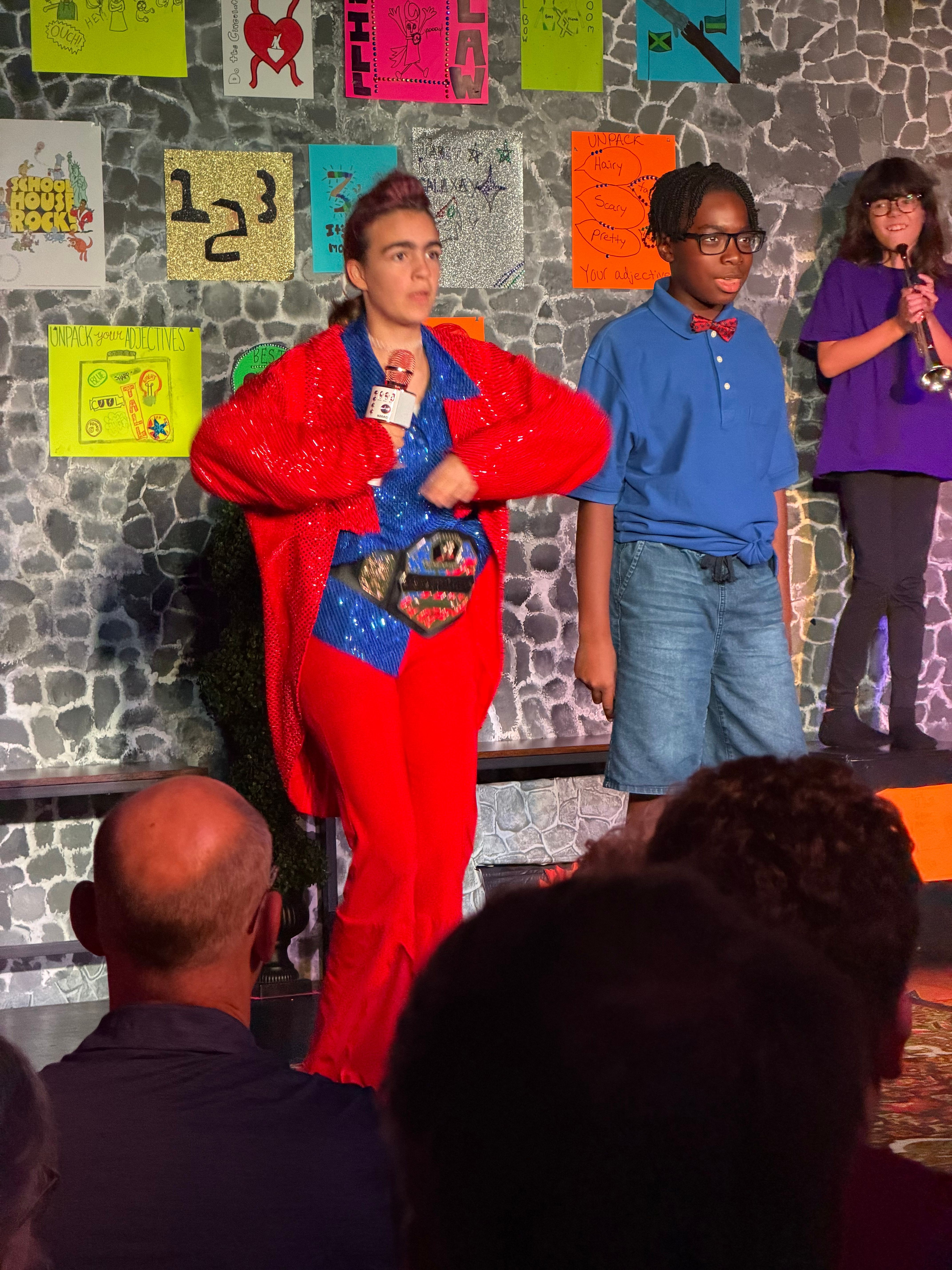 Person in red costume holding a microphone, standing in front of a colorful wall with puzzle piece decorations.