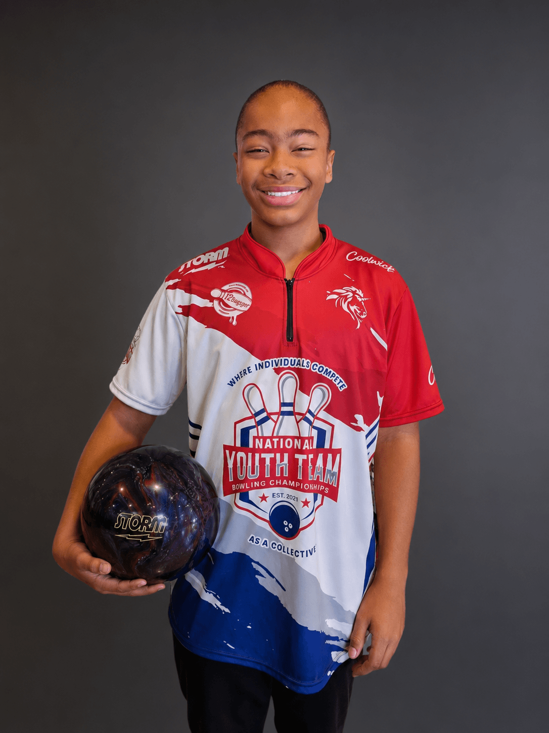 Young person smiling, holding a bowling ball, wearing a sports jersey with logos and text, standing against a dark background.