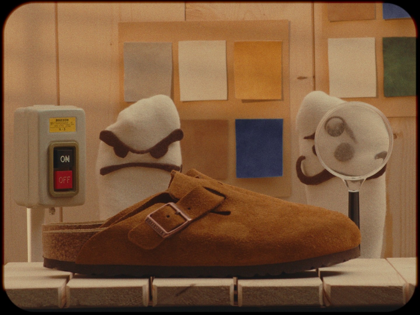 A brown shoe with a buckle on a shelf, with two plush toys behind it, one with sunglasses and one with a round face.