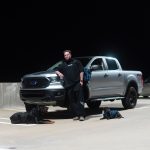 Person standing next to a silver pickup truck on a parking lot at night.