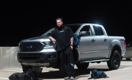 Person standing next to a silver pickup truck on a parking lot at night.