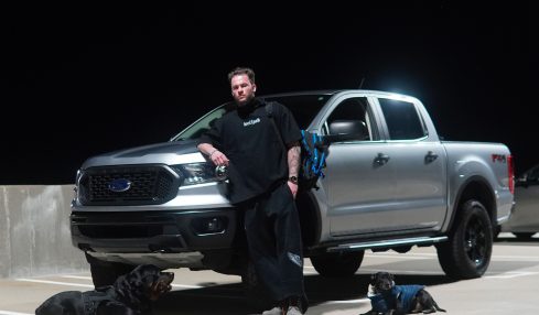 Person standing next to a silver pickup truck on a parking lot at night.