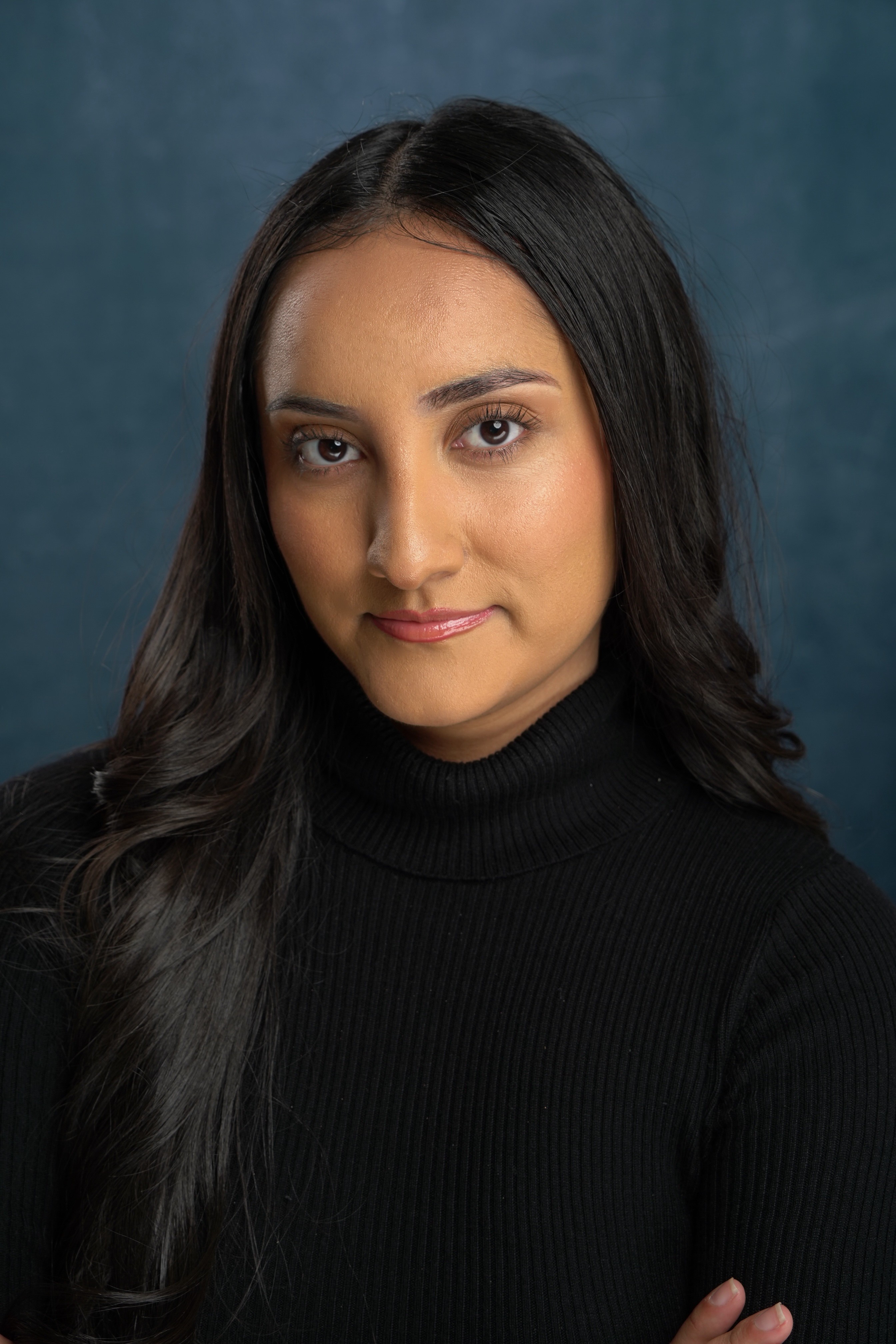 Portrait of a woman with long dark hair wearing a black turtleneck, looking at the camera with a neutral expression.