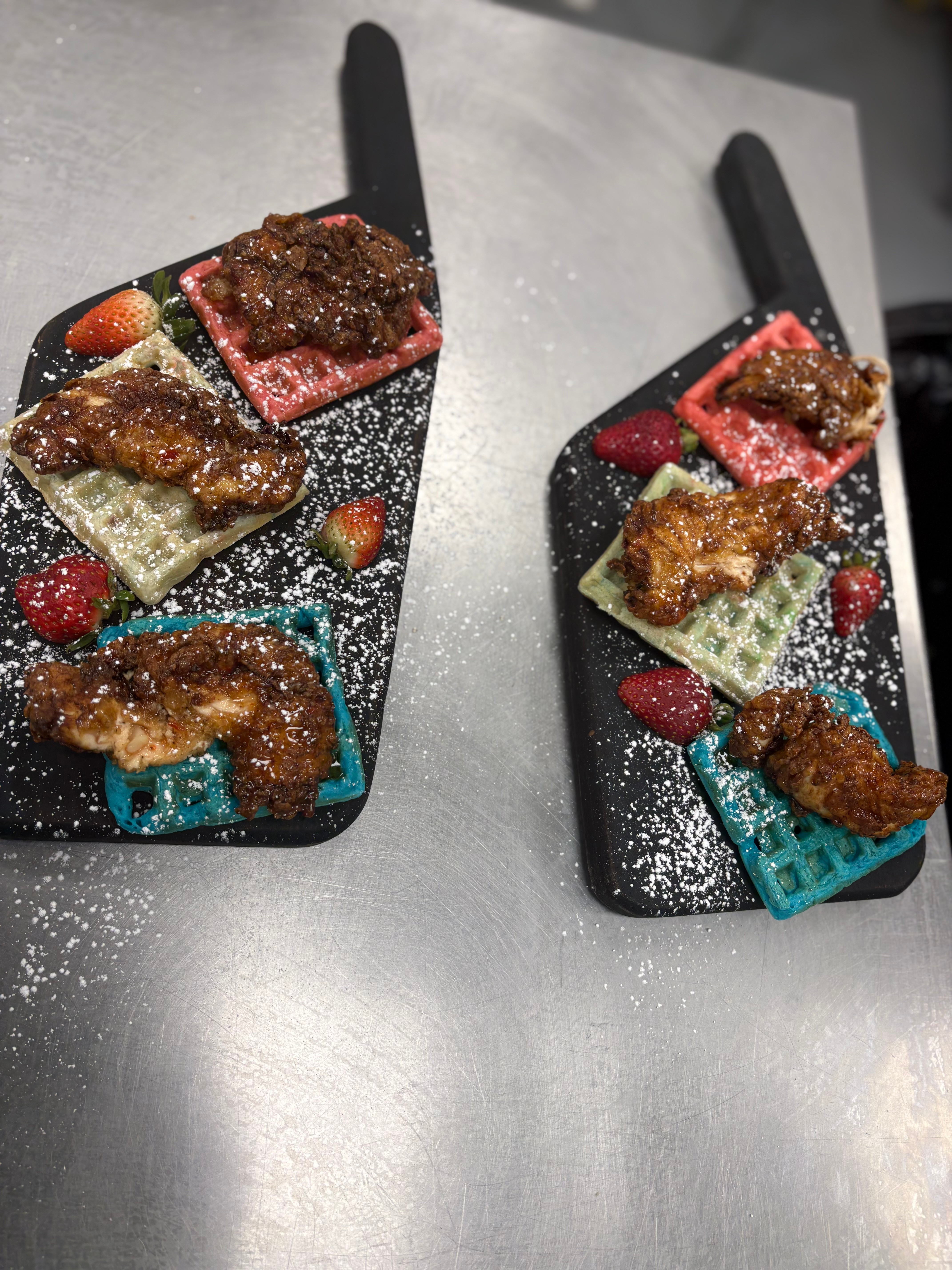 Two black spatulas with colorful toppings and powdered sugar on a metallic surface.