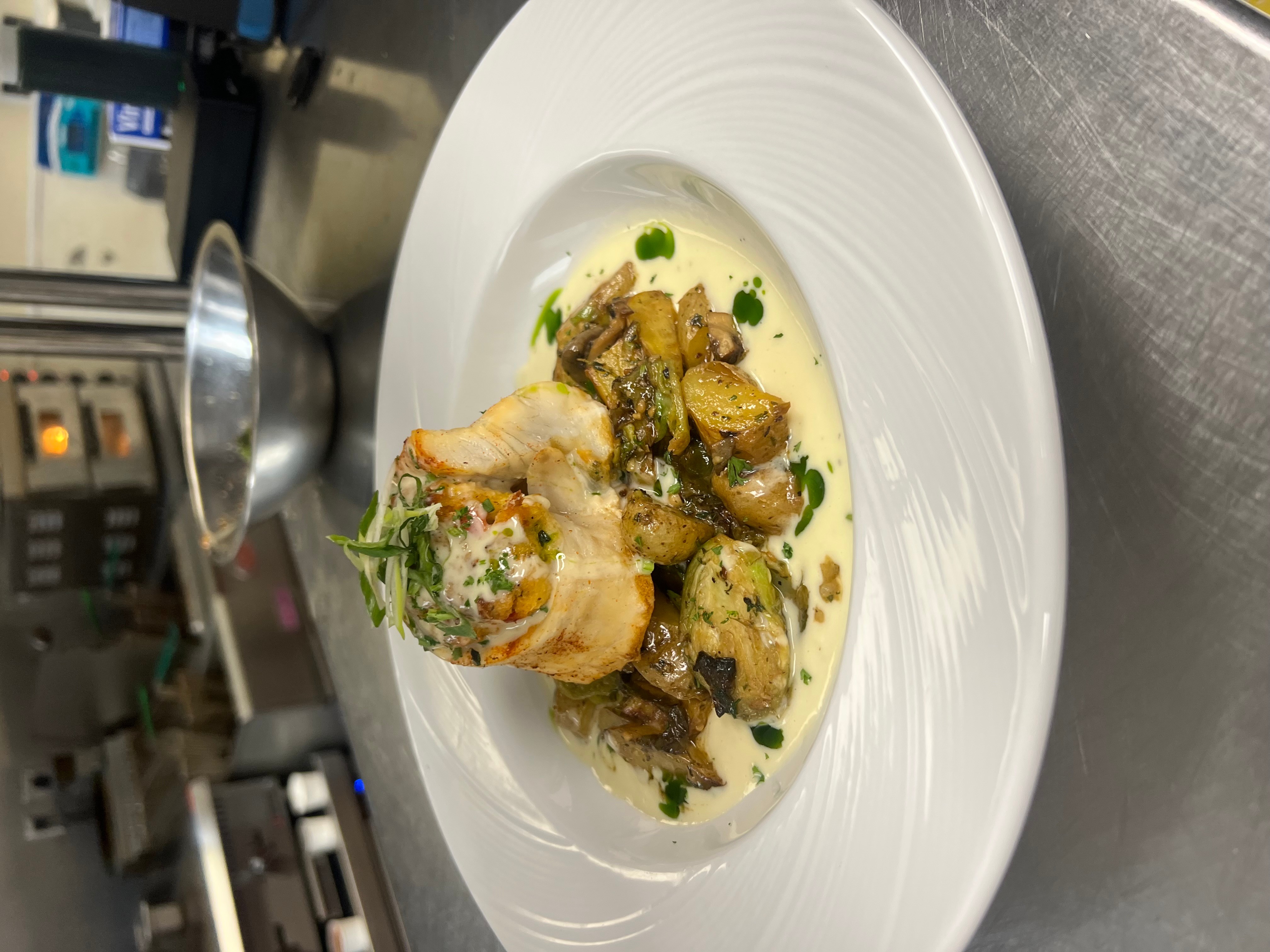 Plate with cooked chicken, roasted vegetables, and green herbs in a creamy sauce, on a white dish.